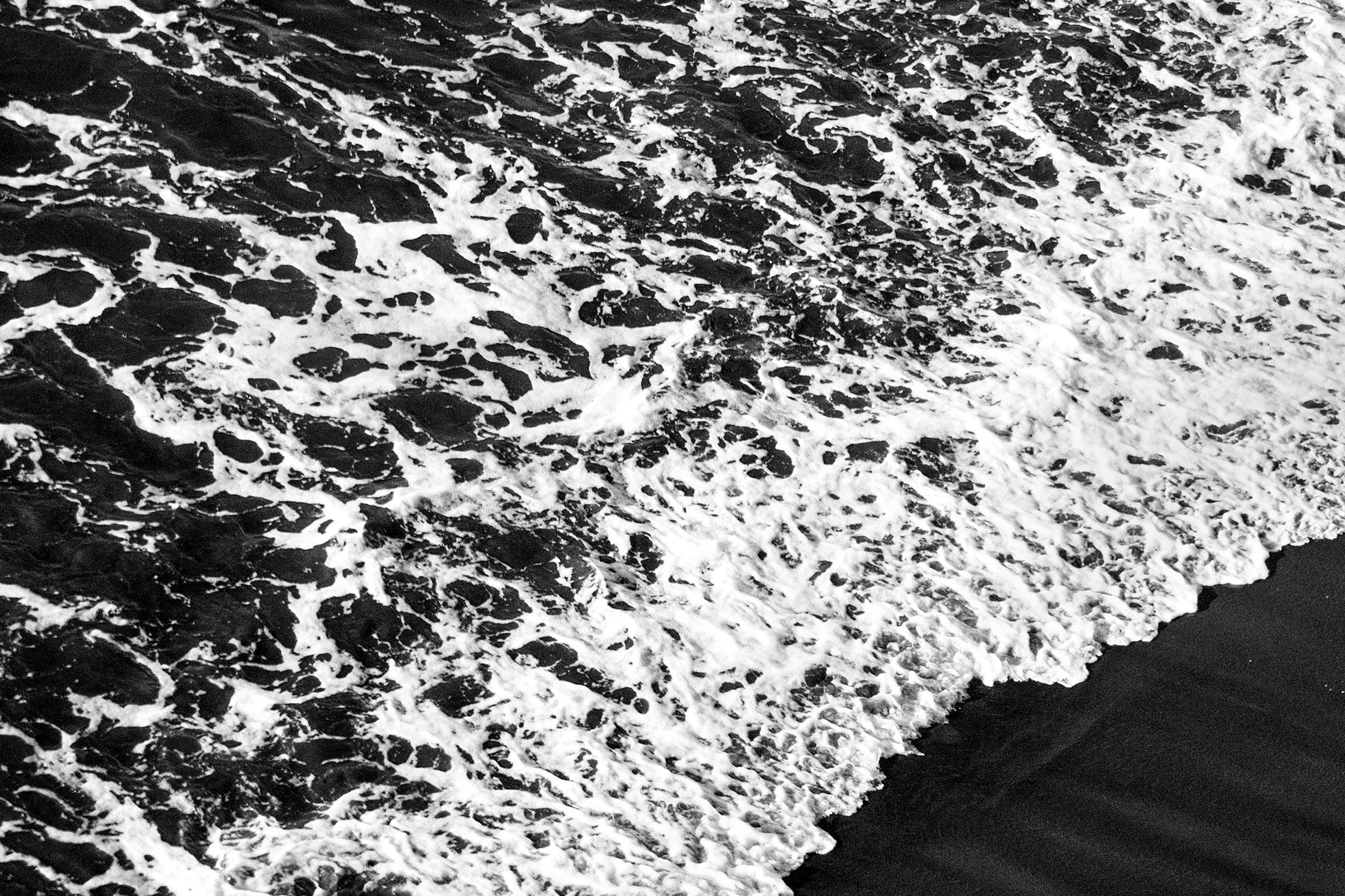 Shore de sable noir profond, paysage marin noir et blanc, vague éclatante qui attire sur la côte - Noir Black and White Photograph par Kind of Cyan