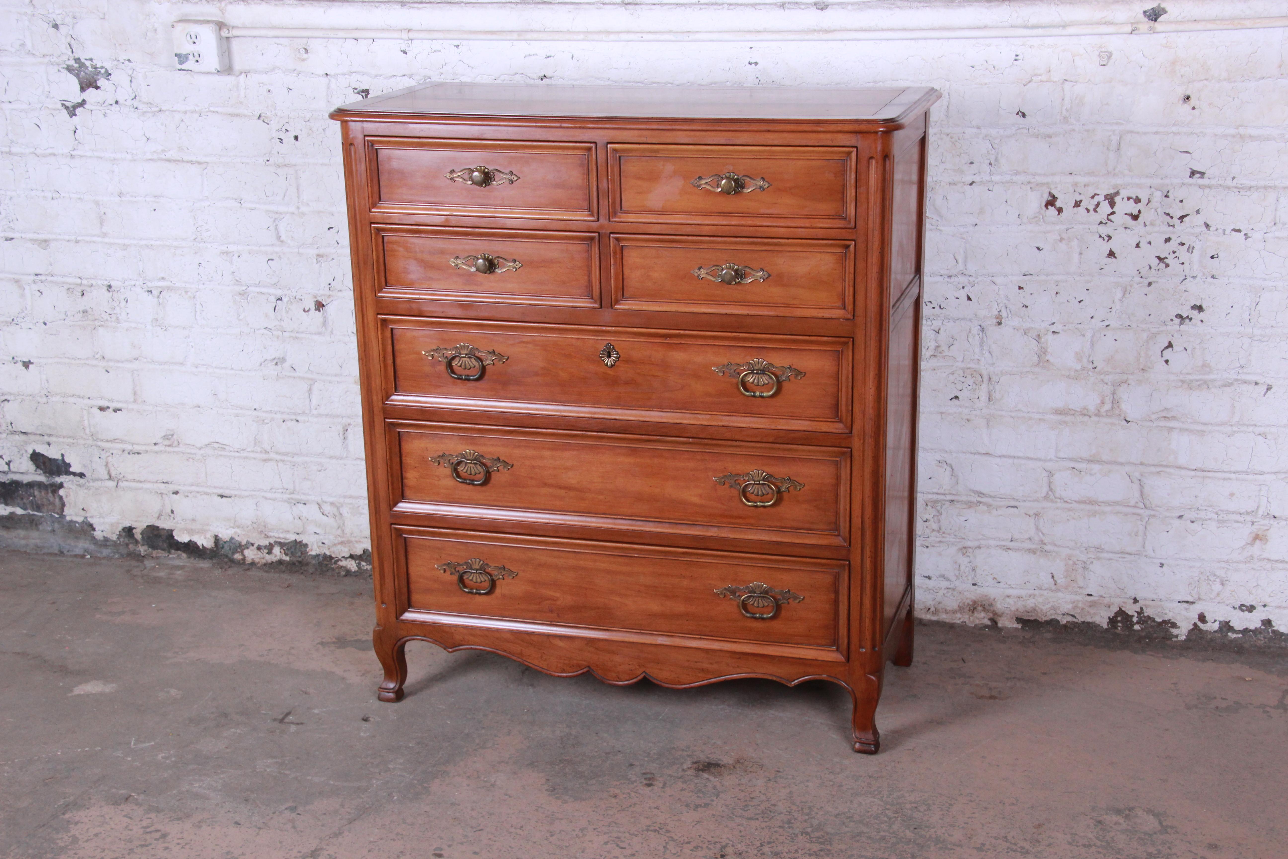 A gorgeous vintage French Provincial highboy dresser by Kindel Furniture of Grand Rapids, MI. The dresser features solid cherrywood construction and beautiful wood grain. It offers ample storage, with seven deep dovetailed drawers. The original