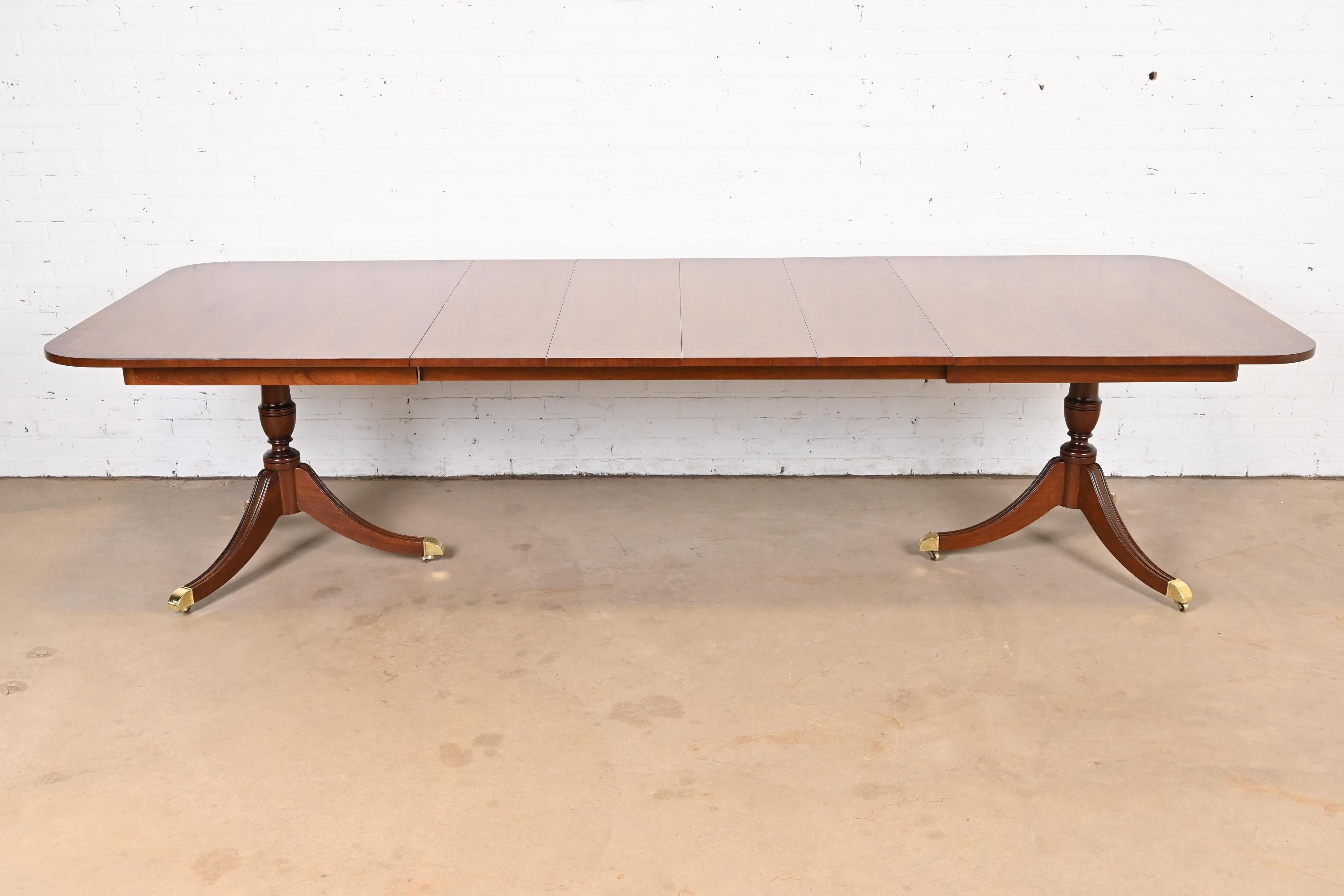 An exceptional Georgian or Regency style double pedestal extension dining table

By Kindel Furniture

USA, Circa 1980s

Gorgeous book-matched mahogany, with satinwood string inlay banding, carved solid mahogany pedestals, brass-capped feet, and
