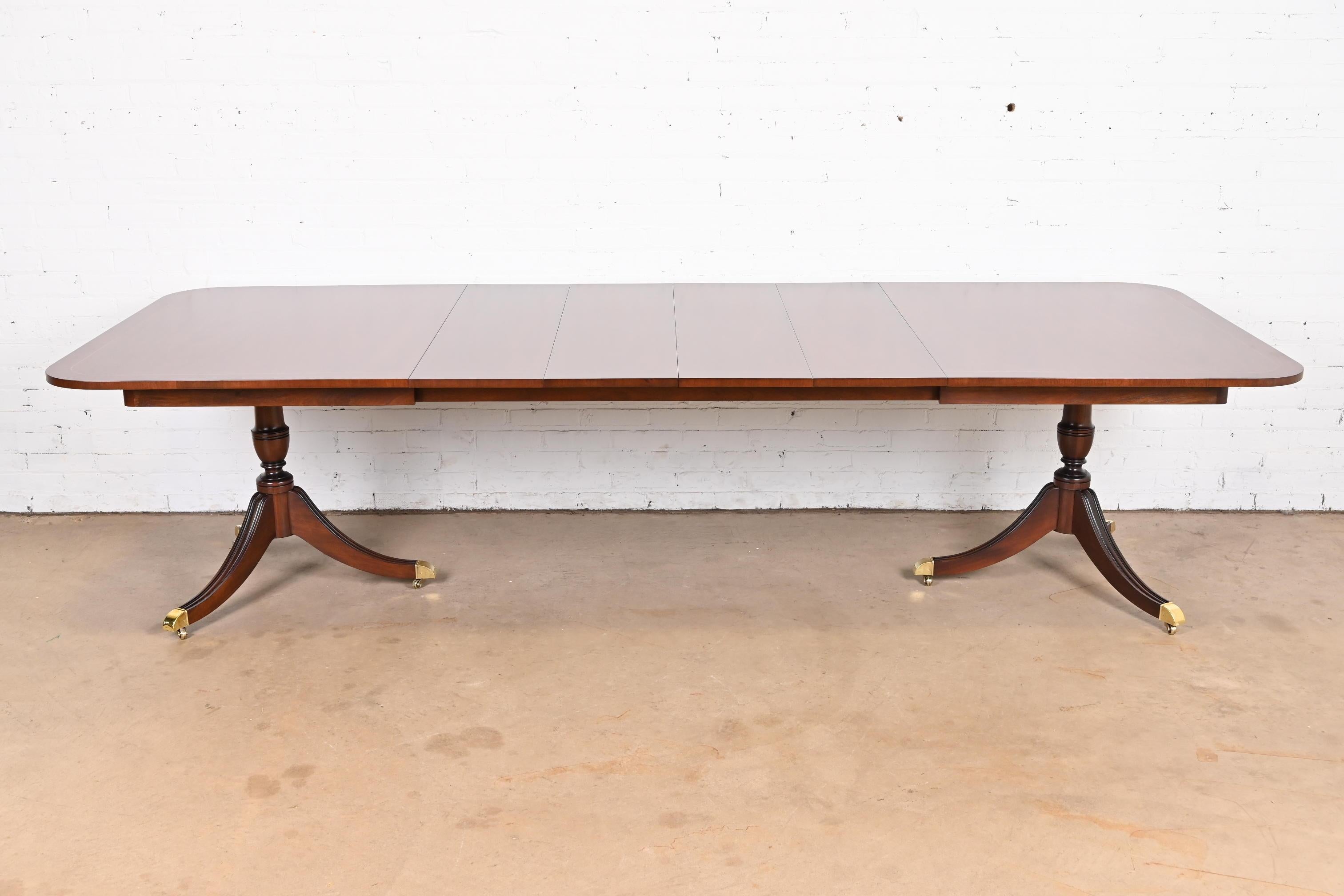 An exceptional Georgian or Regency style double pedestal extension dining table

By Kindel Furniture

USA, Circa 1980s

Gorgeous book-matched mahogany, with satinwood string inlay, carved solid mahogany pedestals, brass-capped feet, and brass