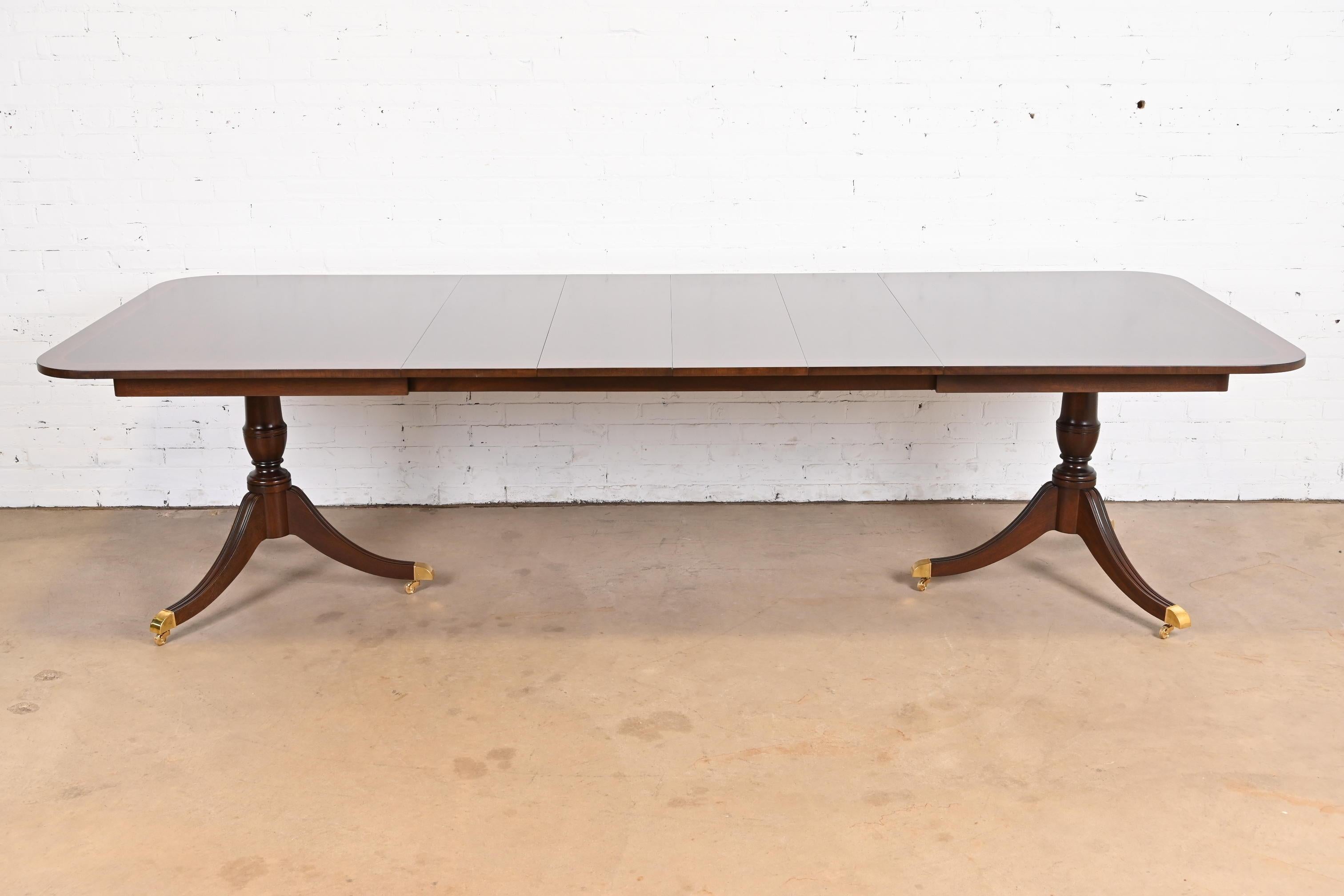 An exceptional Georgian or Regency style double pedestal extension dining table

By Kindel Furniture

USA, Circa 1980s

Book-matched mahogany, with inlaid satinwood banding, carved solid mahogany pedestals, brass-capped feet, and brass