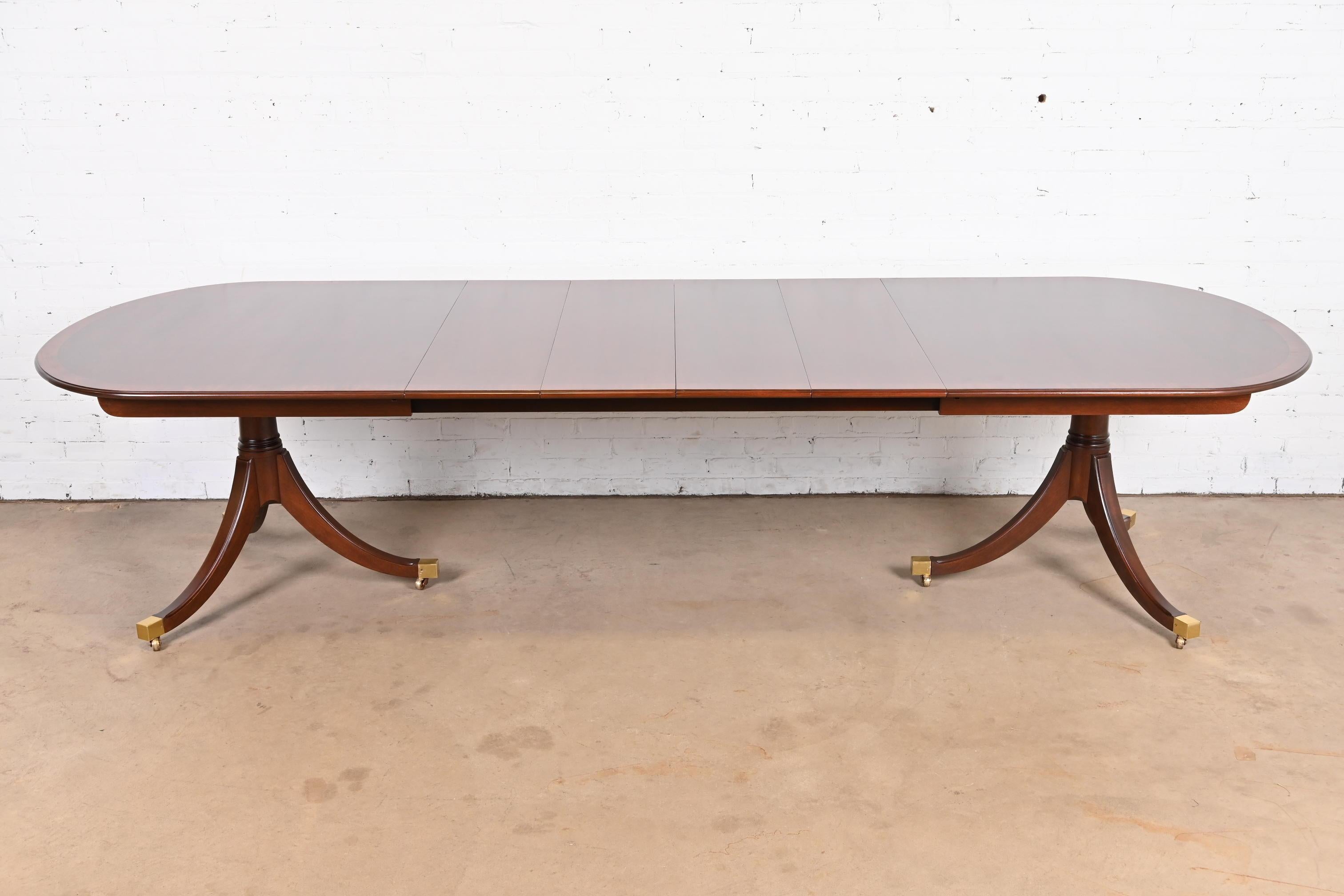 An exceptional Georgian or Regency style double pedestal extension dining table

By Kindel Furniture

USA, Circa 1980s

Gorgeous book-matched mahogany, with satinwood banding, carved solid mahogany pedestals, brass-capped feet, and brass