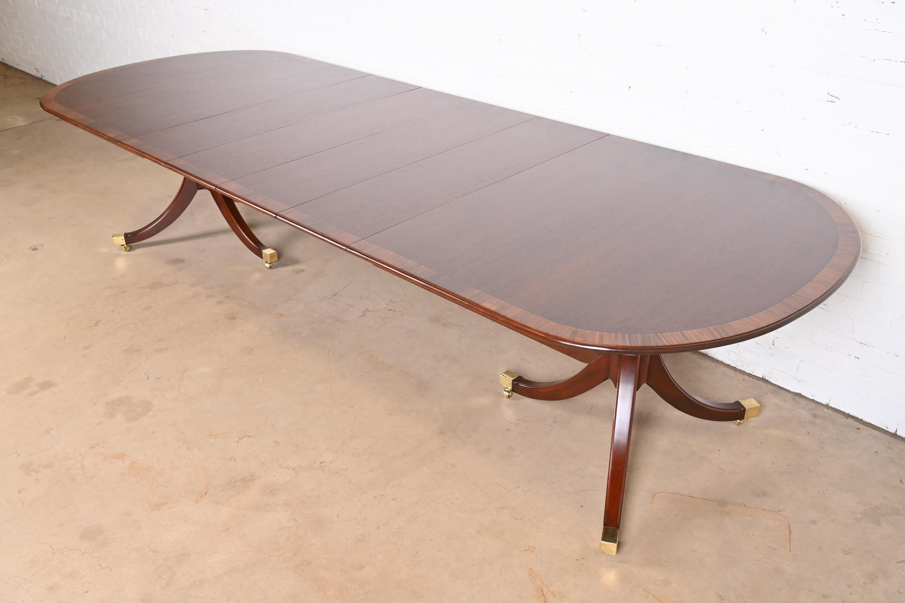 An exceptional Georgian or Regency style double pedestal extension dining table

By Kindel Furniture

USA, Circa 1980s

Gorgeous book-matched mahogany, with satinwood banding, carved solid mahogany pedestals, brass-capped feet, and brass