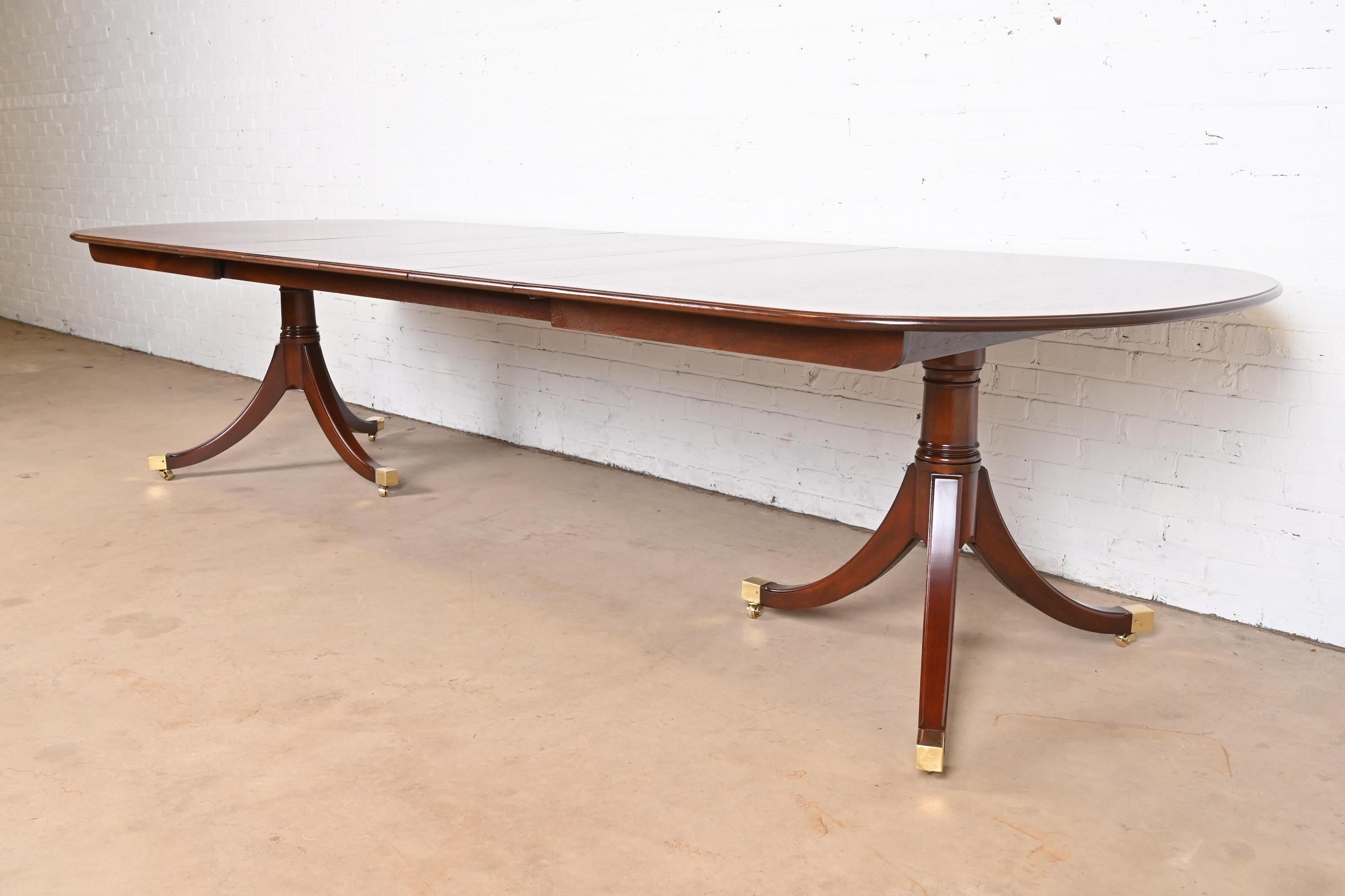 An exceptional Georgian or Regency style double pedestal extension dining table

By Kindel Furniture

USA, Circa 1980s

Gorgeous book-matched mahogany, with satinwood banding, carved solid mahogany pedestals, brass-capped feet, and brass