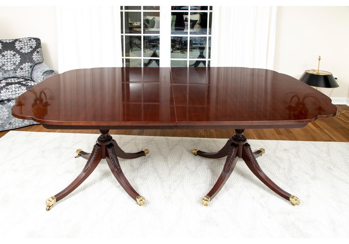 Kindel Furniture Georgian style mahogany double pedestal dining table featuring scalloped top with two pedestals carved with acanthus leaves and ribbed legs ending in wonderful brass paw feet on casters. Table comes with four additional self-storing