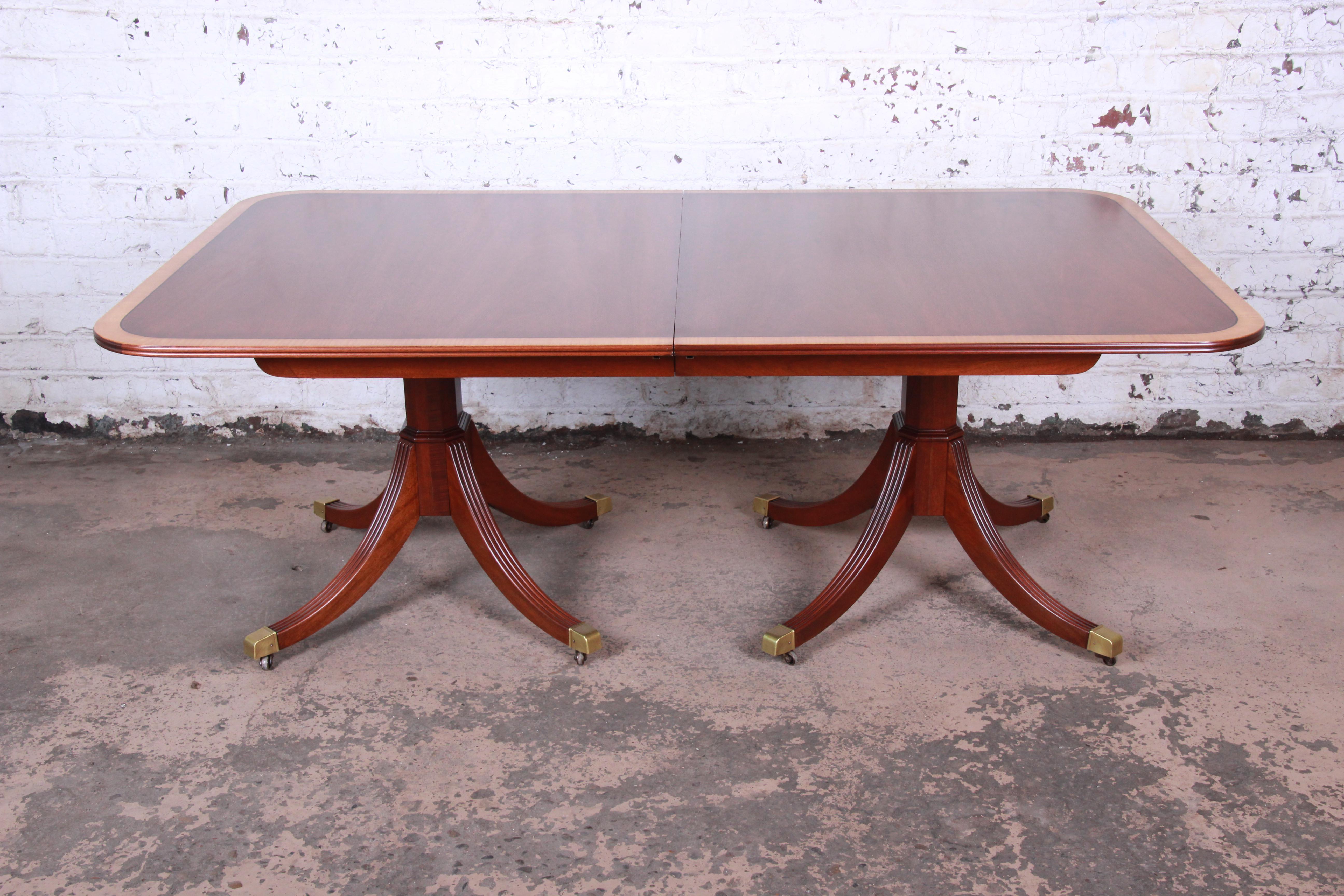 An exceptional banded mahogany double pedestal extension dining table by Kindel Furniture. The table features gorgeous mahogany wood grain with a beautiful banded edge. It sits on two pedestals with four fluted legs with brass-tipped feet. The table