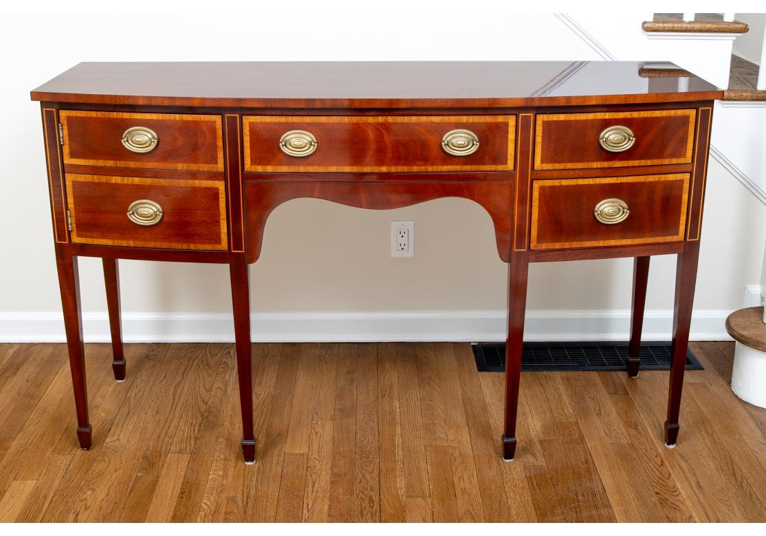 A handsome and very well made Kindel Mahogany  bow front sideboard featuring three  banded drawer fronts with oval brass pulls, one with flatware tray and false double drawer cabinet door which opens to reveal an interior shelf. Raised on square