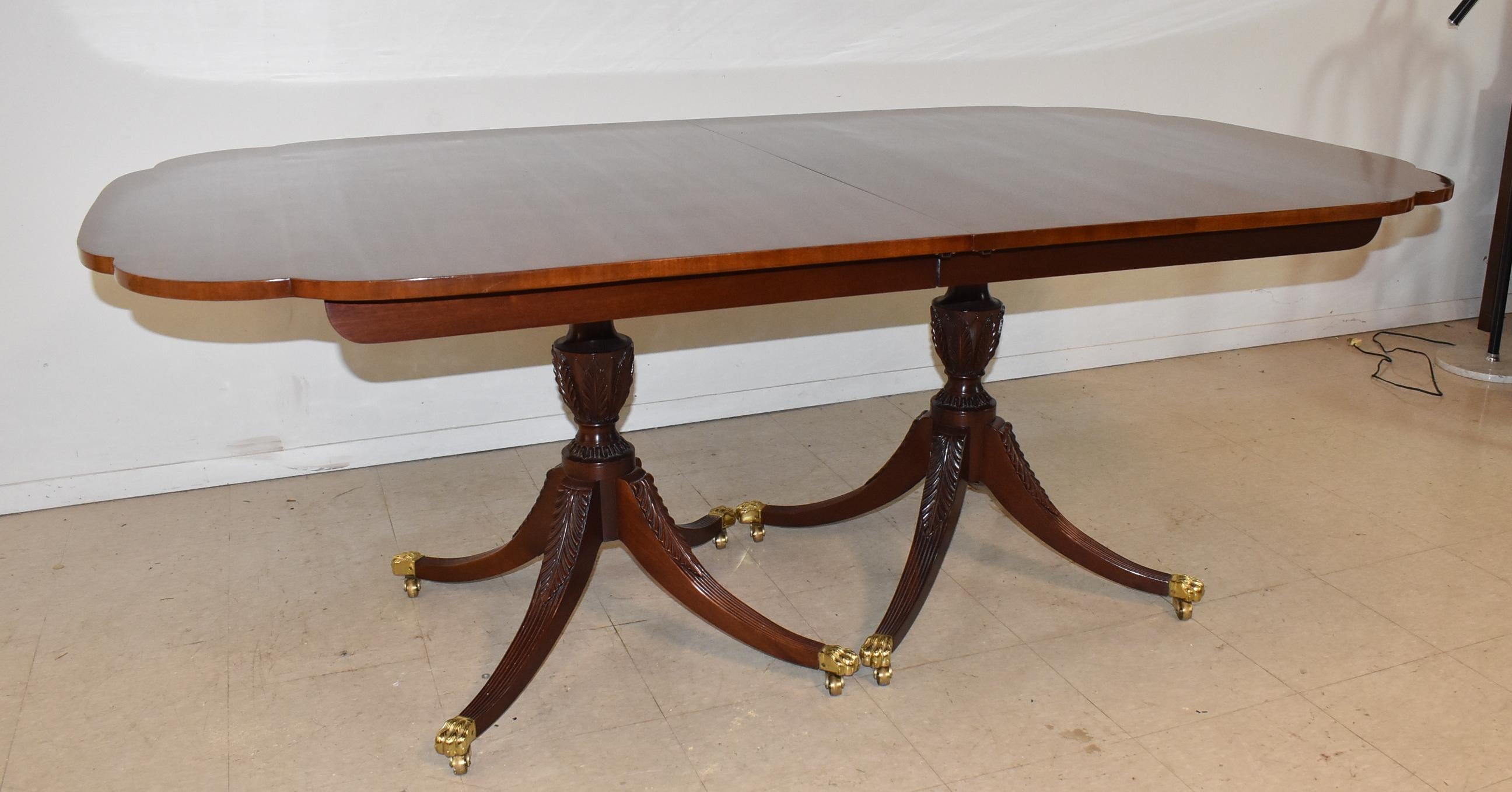 Cette magnifique table de salle à manger en acajou de la série Winterthur de Kindel présente des coins festonnés uniques et la finition originale de la couleur de préservation. Les piédestaux en forme d'urne sont sculptés à la main avec des feuilles