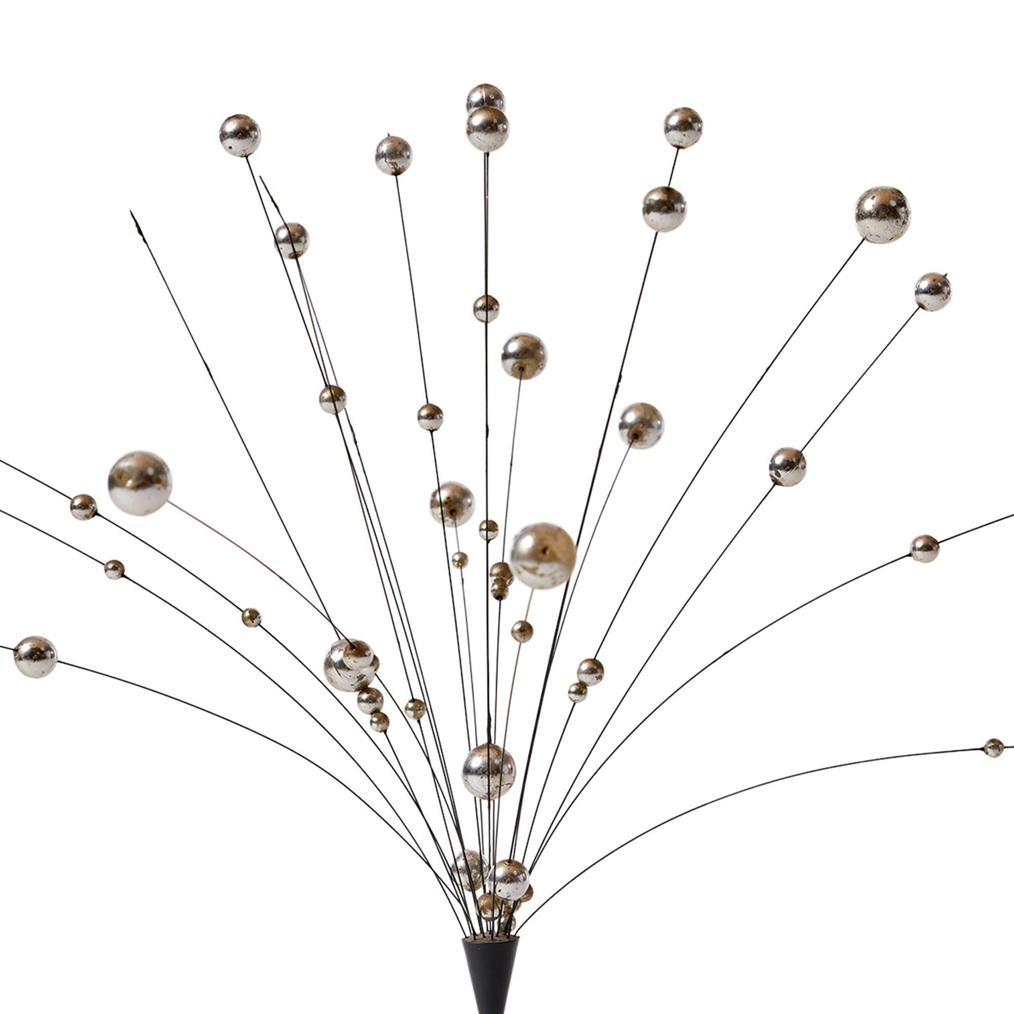 A kinetic sculpture comprised of variegated balls on undulating wire rods stemming from a metal pedestal.