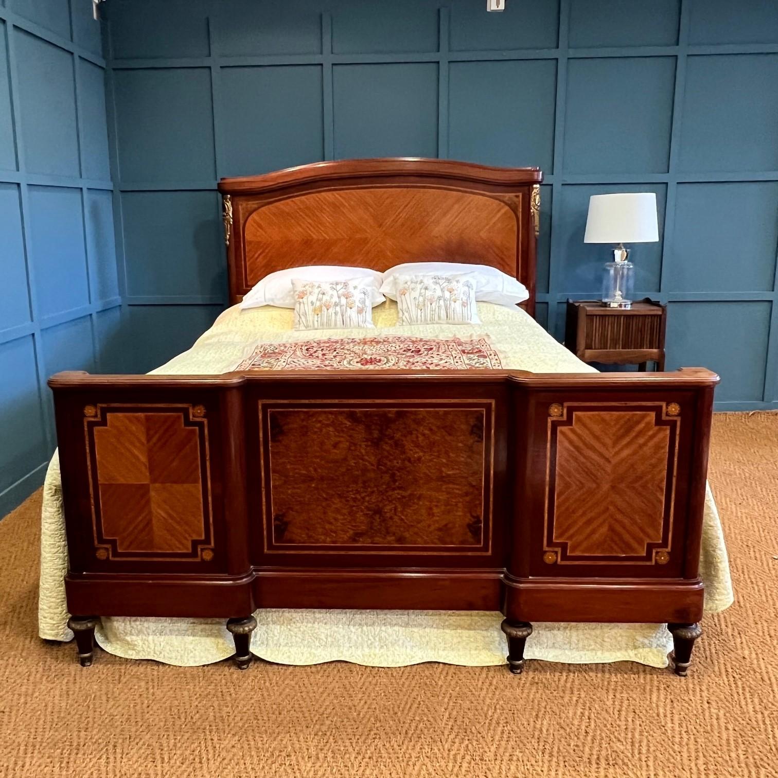 Handsome King size French bedstead with burr walnut central panel marquetry and fruitwood frames encompasses further marquetry on the foot end. The bed head has central marquetry edged with ormulu gilded bronze decorations. The turned feet are edged