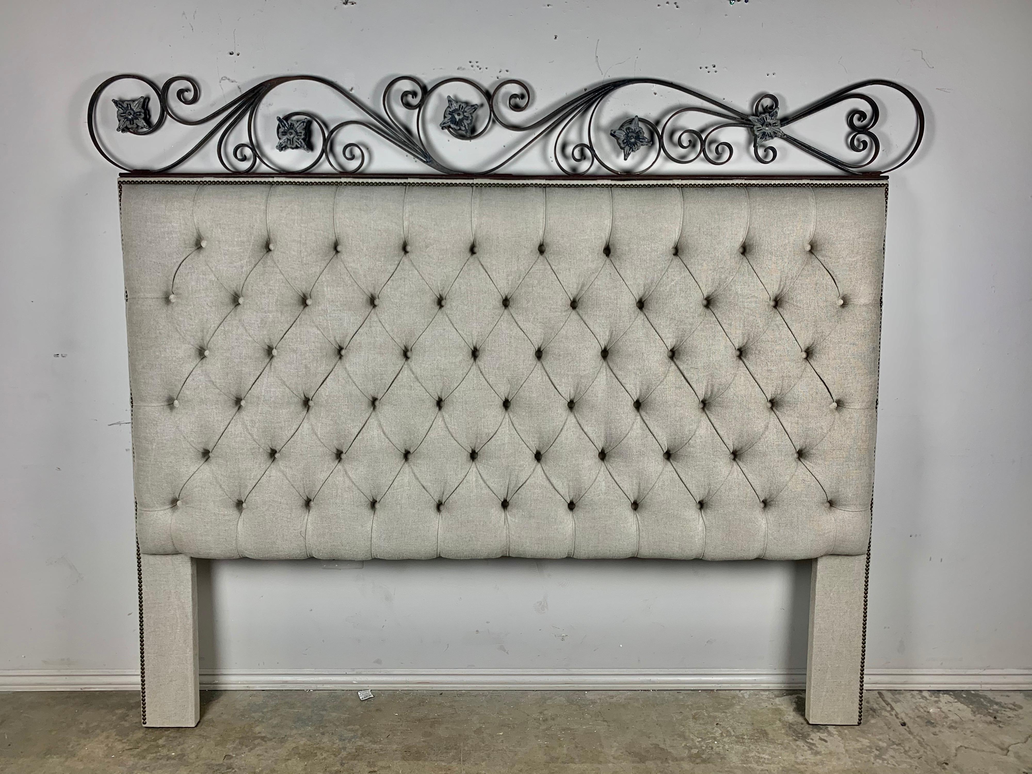 Custom King size Belgium linen tufted headboard. The headboard is crowned with beautiful scrolled ironwork depicting flowers. Antique brass nailhead trim detail.