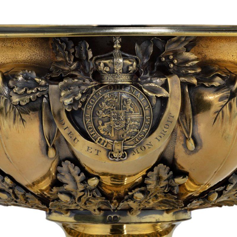 A large circular silver-gilt footed bowl with two handles on either side in the form of a ship’s prow, one with a crowned lion, the other with a unicorn wearing a chain of office, the sides with four vegetal forms interleaved with acorn bearing oak