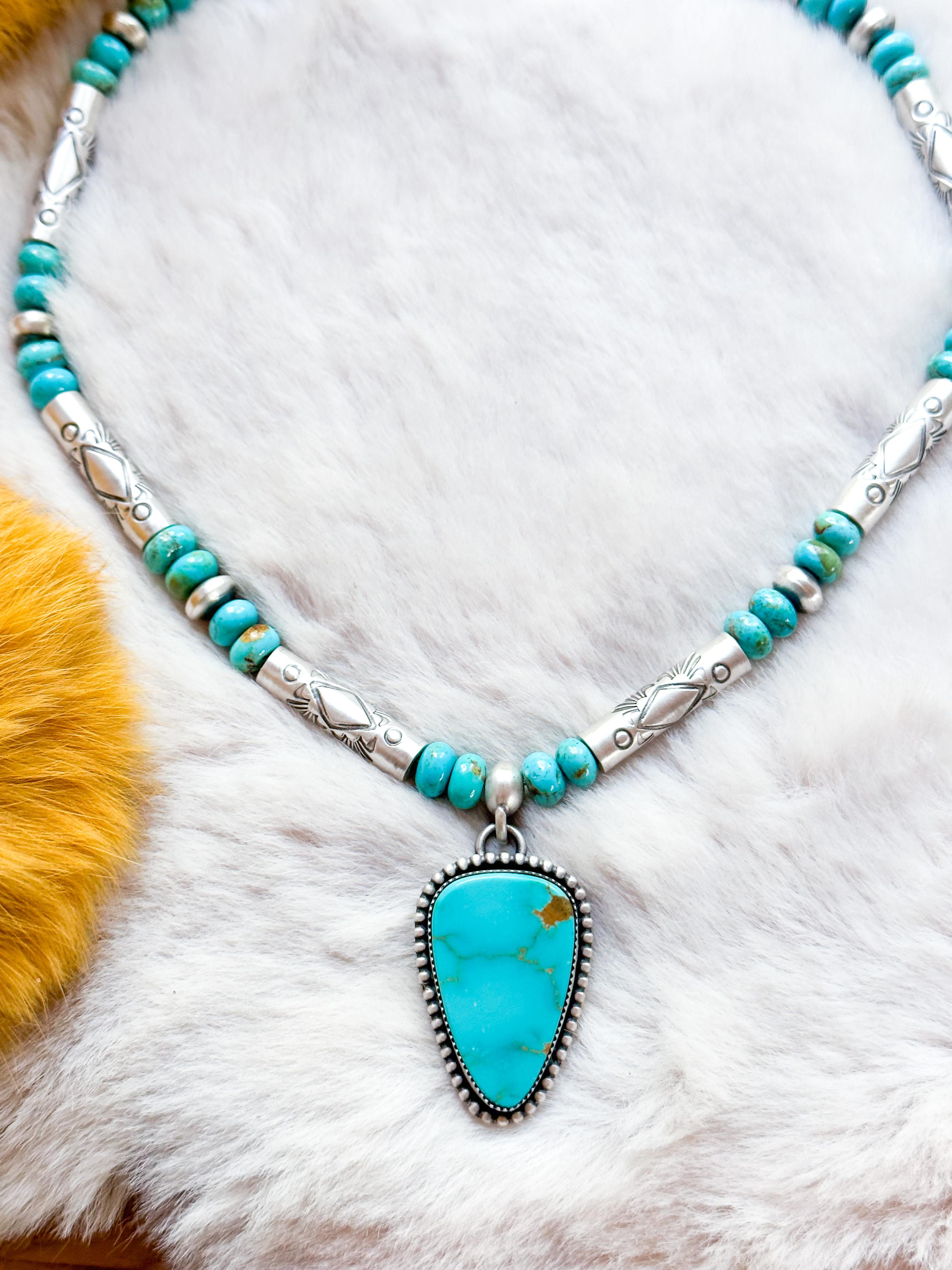 Unsere bezaubernde, handgeprägte türkisfarbene Perlenkette ist eine auffallende Verschmelzung von lebhaften Blau- und Grüntönen, die mit schimmernden Silberperlen verziert sind. Dieses exquisite Stück wird von einem faszinierenden dreieckigen