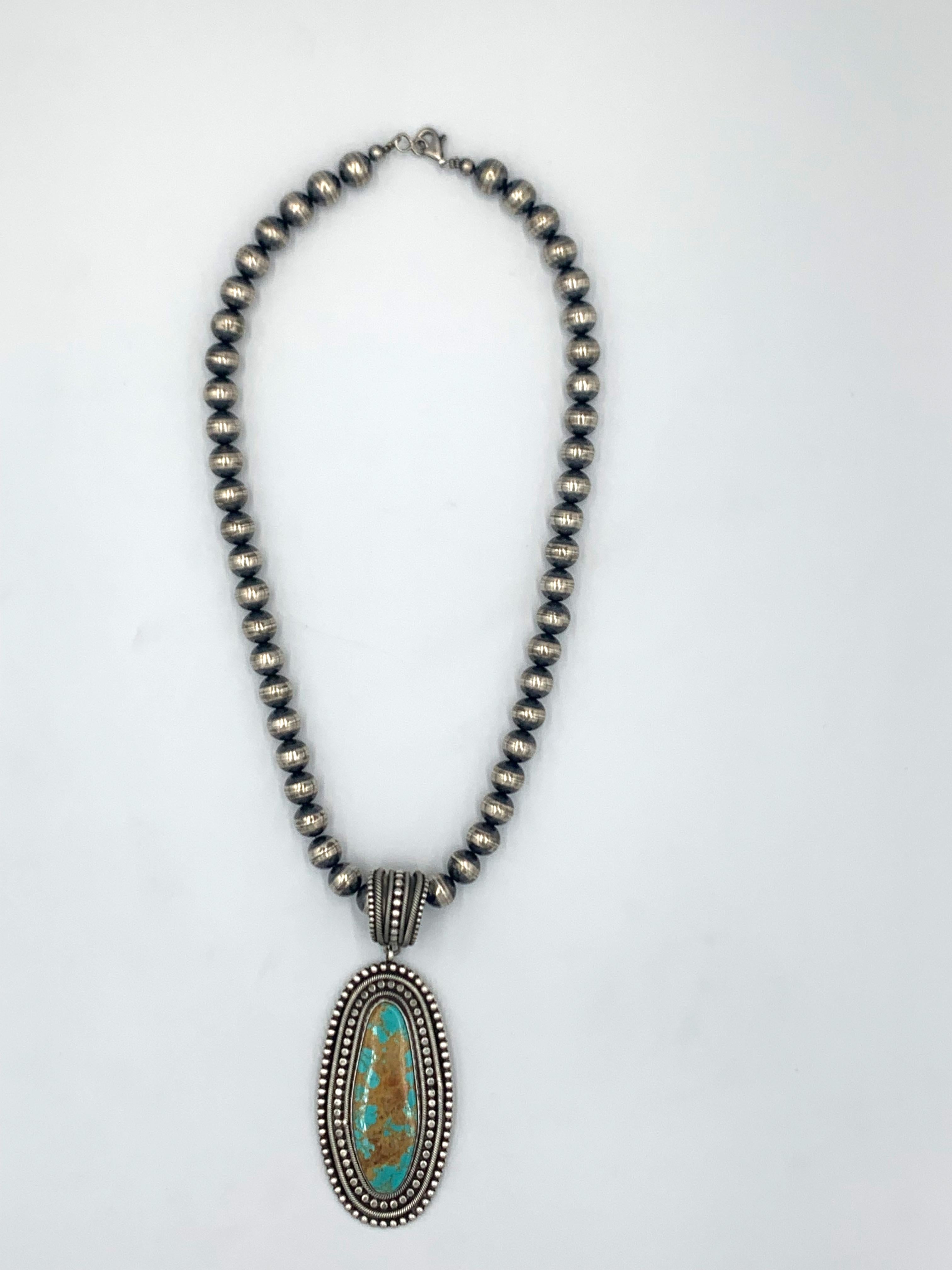 King’s Manassa turquoise pendant is made by Navajo silversmith Rick Martinez. The 1 1/2” x 3” sterling silver pendant has a 3/4” x 2 1/8” turquoise stone bordered by silver applique raindrops. A 7/8” matching bale makes a total length of 4”. It is