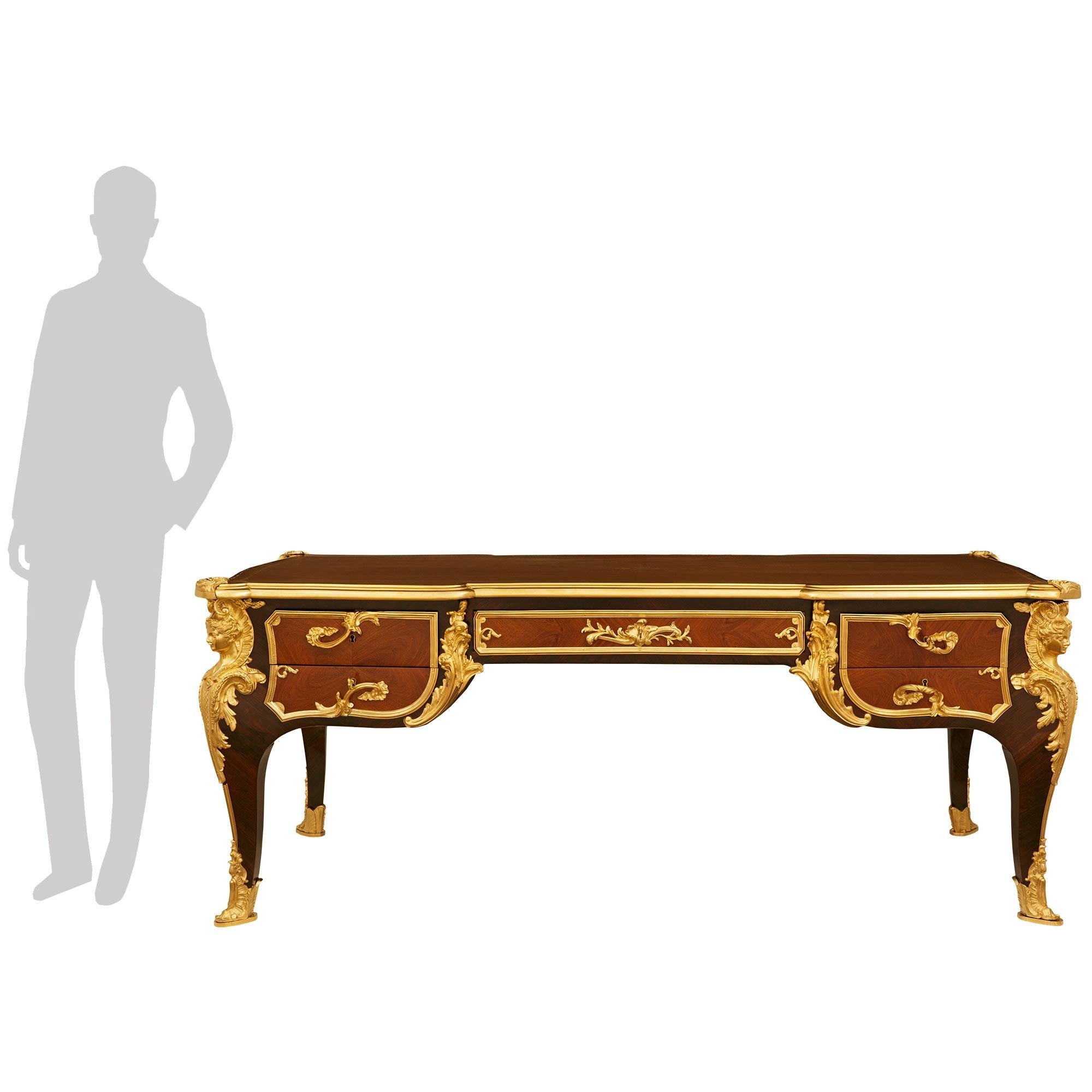 An important and most handsome French 19th century Louis XV st. Kingwood, Tulipwood and Ormolu desk, modeled after Charles Cressent. This stunning Bureau Plat desk is attributed to cabinetmaker E. Kahn & Cie, and is raised by four impressive
