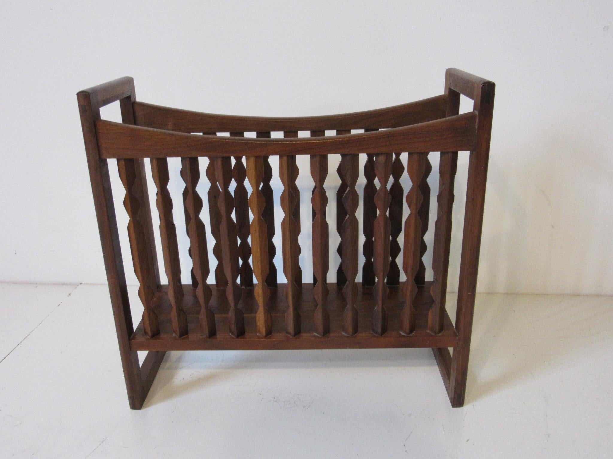 A walnut magazine rack with sculptural spindles to the sides and higher open boxed ends that serve as handles. A sturdy place to keep your reading materials organized, manufactured by the Drexel Furniture Company .