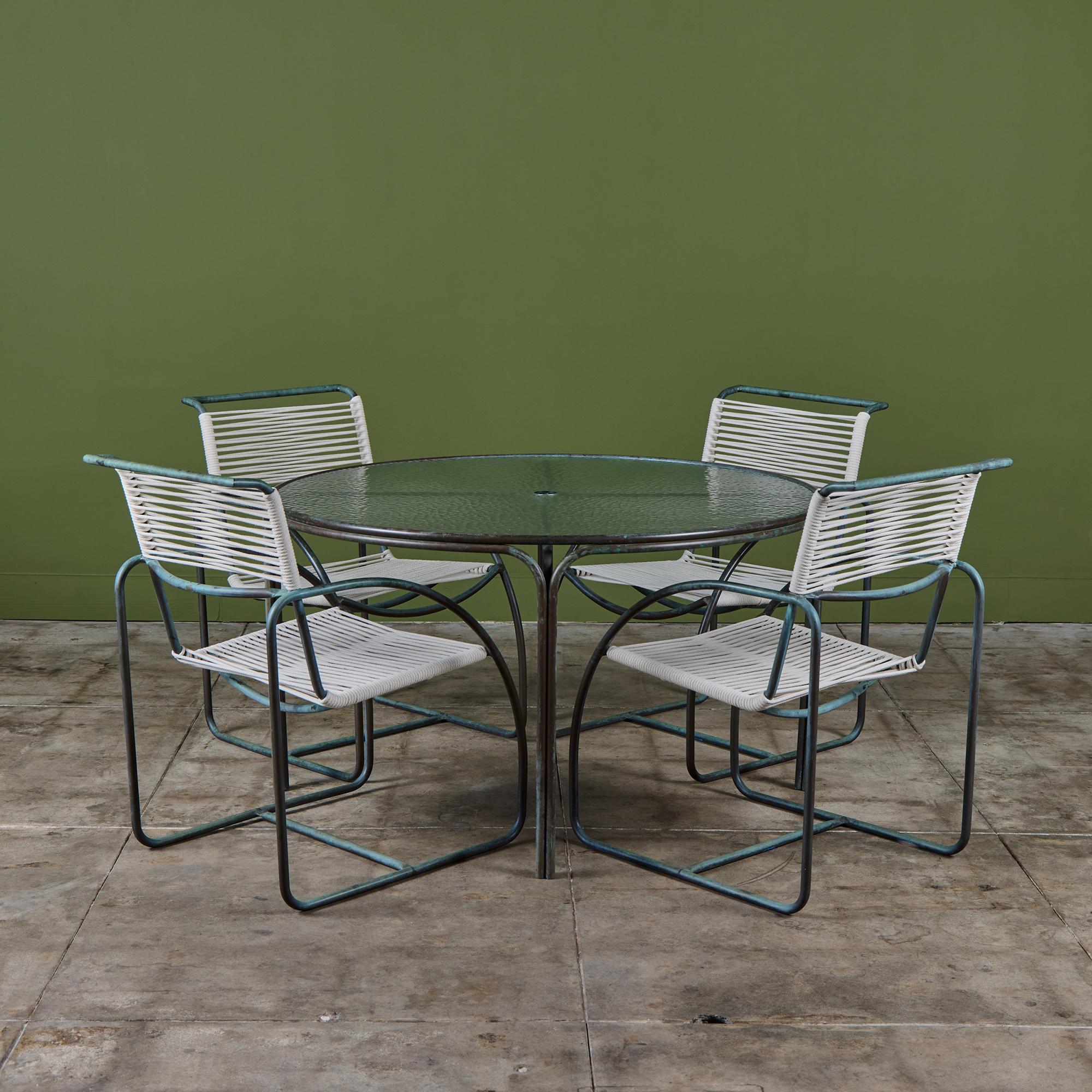 Patio dining set by Kipp Stewart for Terra of California, USA, c.1970s. The set features four patinated bronze tube framed armchairs with matching bronze table, with original pebble glass top. The glass table top has an opening for an umbrella. The
