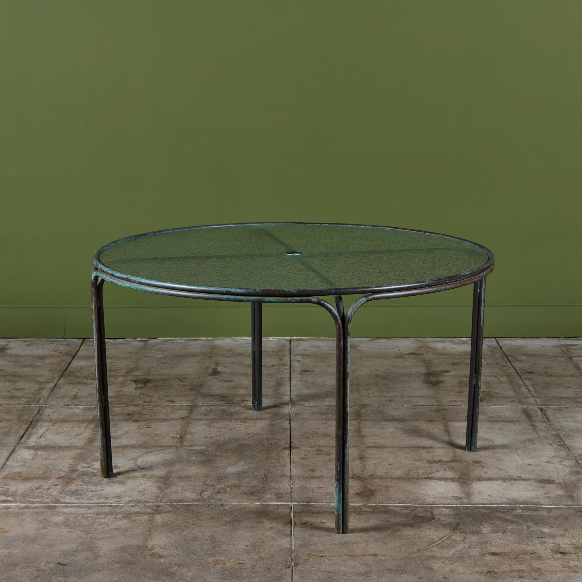 Patio dining table by Kipp Stewart for Terra of California, USA, c.1970s. The table features a bronze tube frame with original pebble glass top and center hole for a patio umbrella.
 
Dimensions
48.5” diameter x 27.25” height.
 
Condition
Good