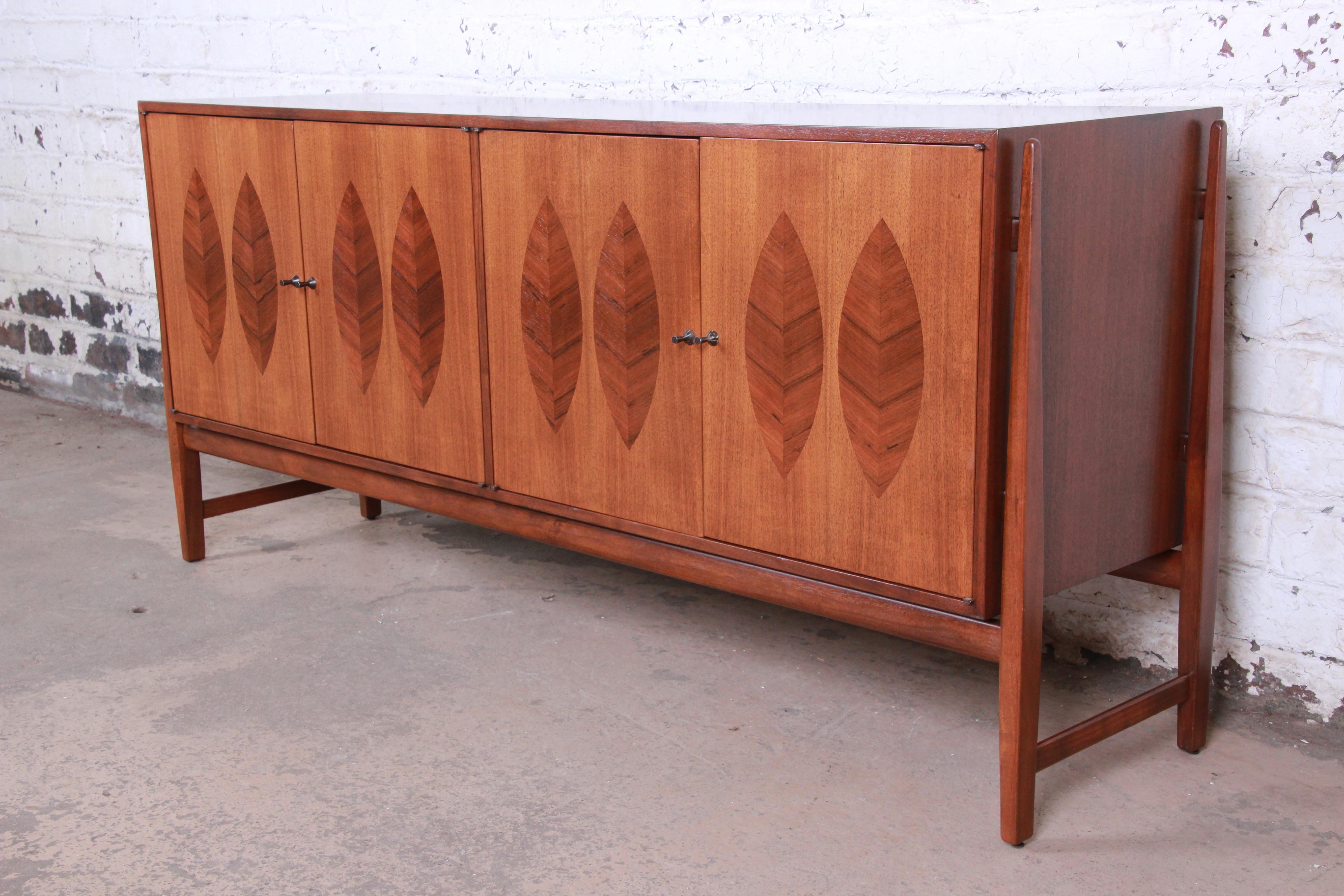 An exceptional Mid-Century Modern credenza or bar cabinet designed by Kipp Stewart for his American Design Foundation line for Calvin Furniture. The credenza features stunning walnut wood grain with leaf inspired rosewood inlays. It offers ample