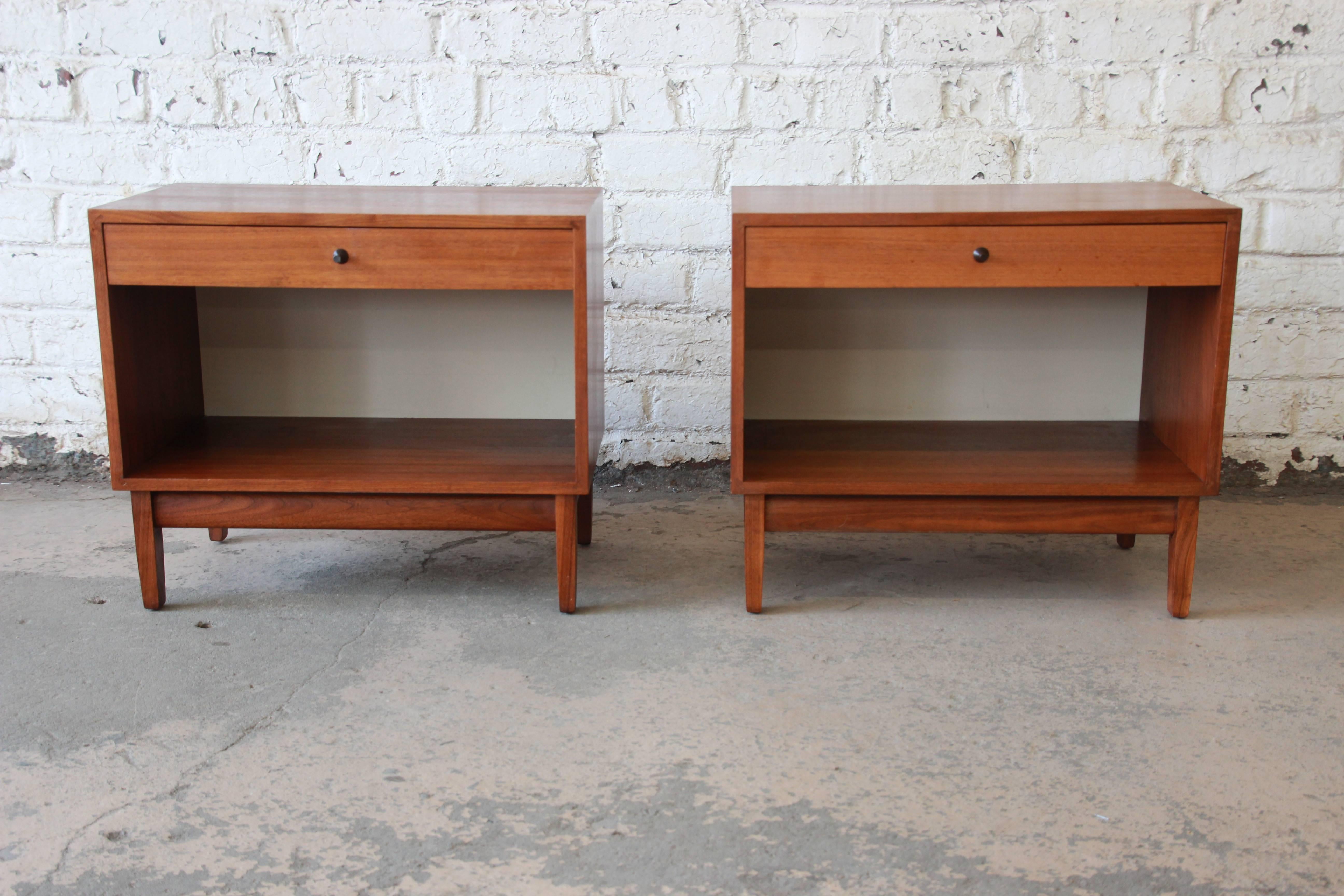An outstanding pair of Mid-Century Modern walnut nightstands designed by Kipp Stewart for his American Design Foundation line for Calvin Furniture, circa 1950s. The nightstands feature gorgeous walnut wood grain and sleek mid-century design. They