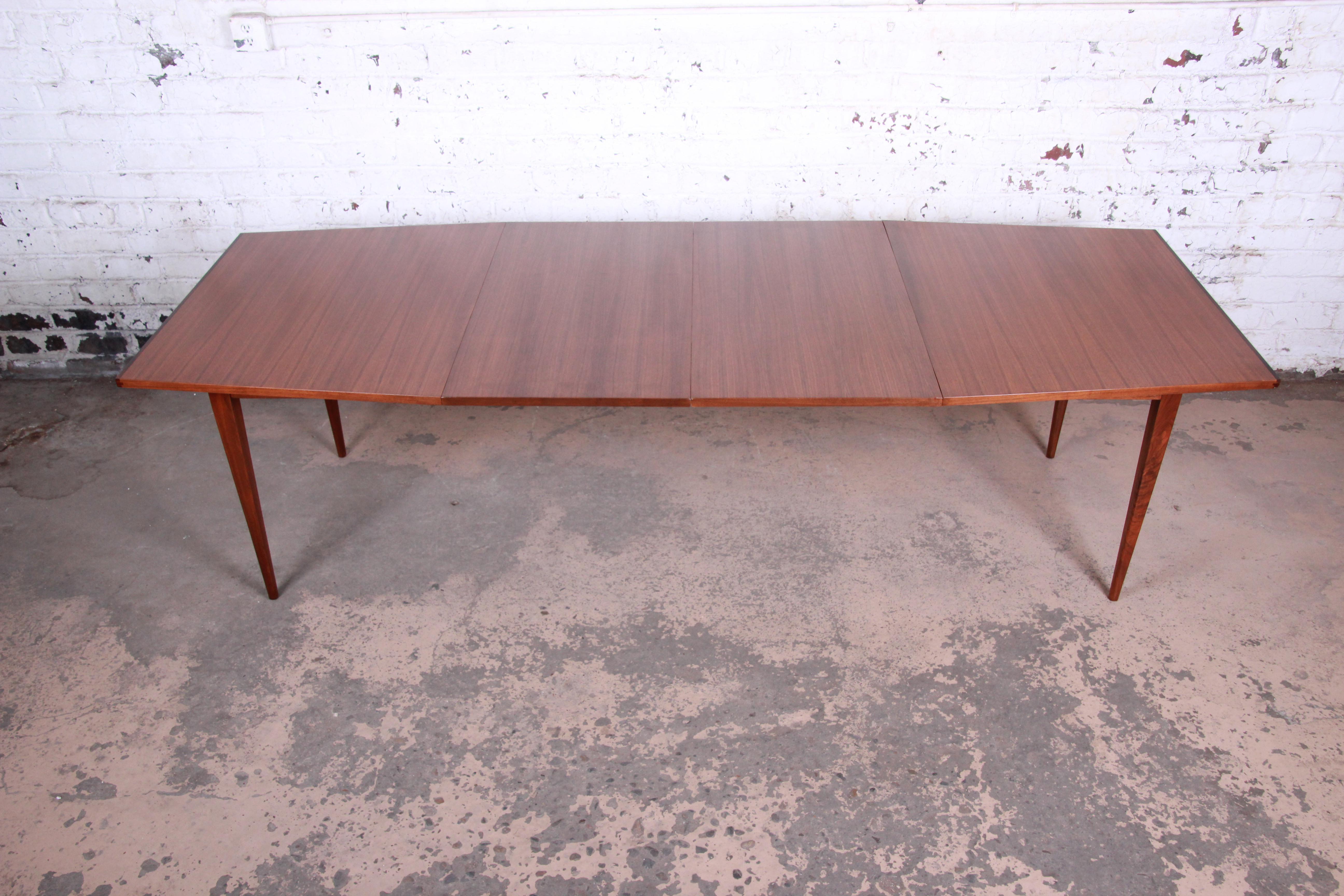 A rare and exceptional Mid-Century Modern boat-shaped extension dining table designed by Kipp Stewart for his American Design Foundation line for Calvin Furniture. The table features stunning walnut wood grain with rosewood edges, tapered solid