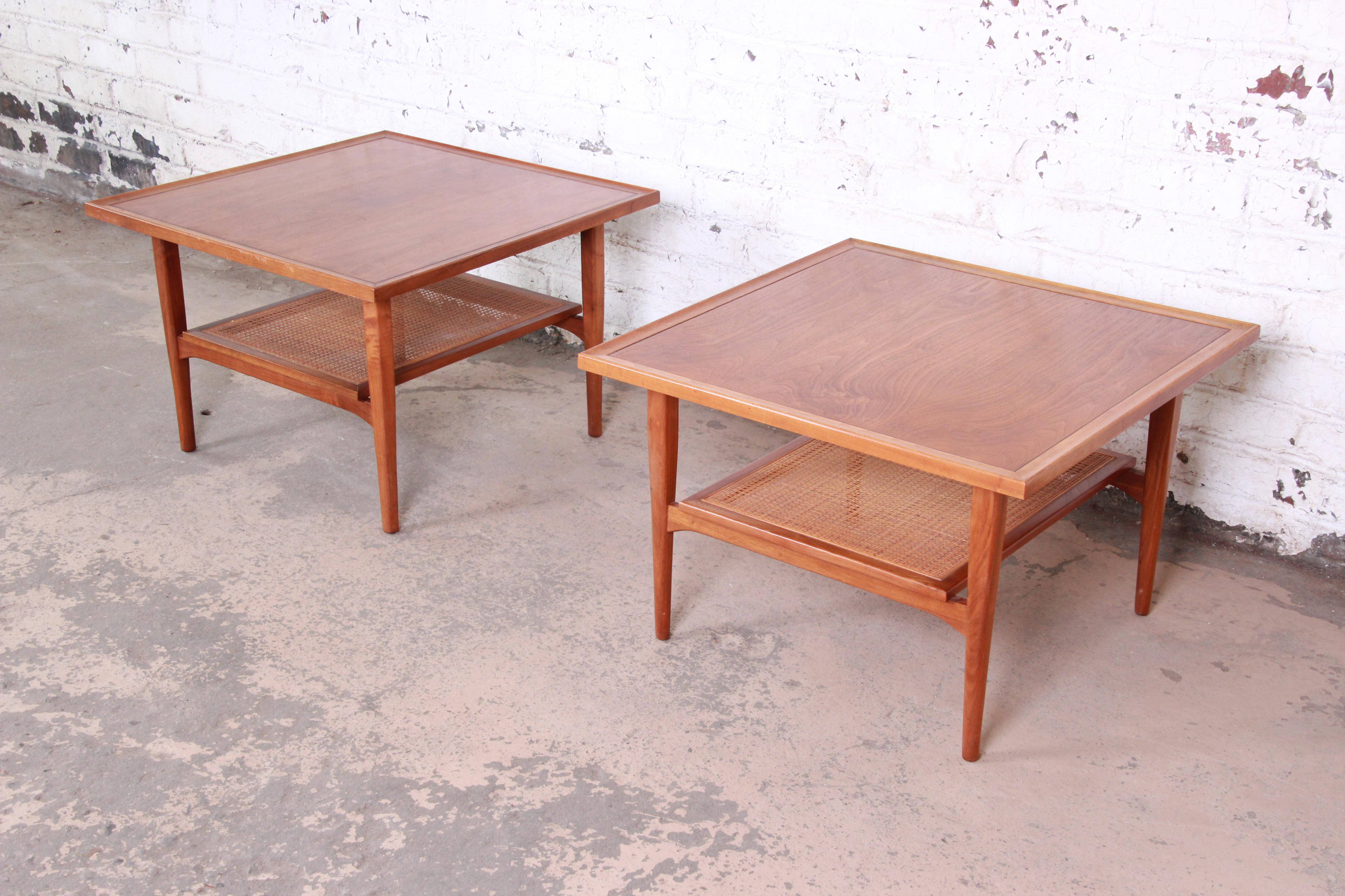 A stunning pair of Mid-Century Modern walnut side tables designed by Kipp Stewart for his Declaration line for Drexel. The tables feature gorgeous walnut wood grain and sleek, Minimalist mid-century design. They have a nice woven bottom shelf, and