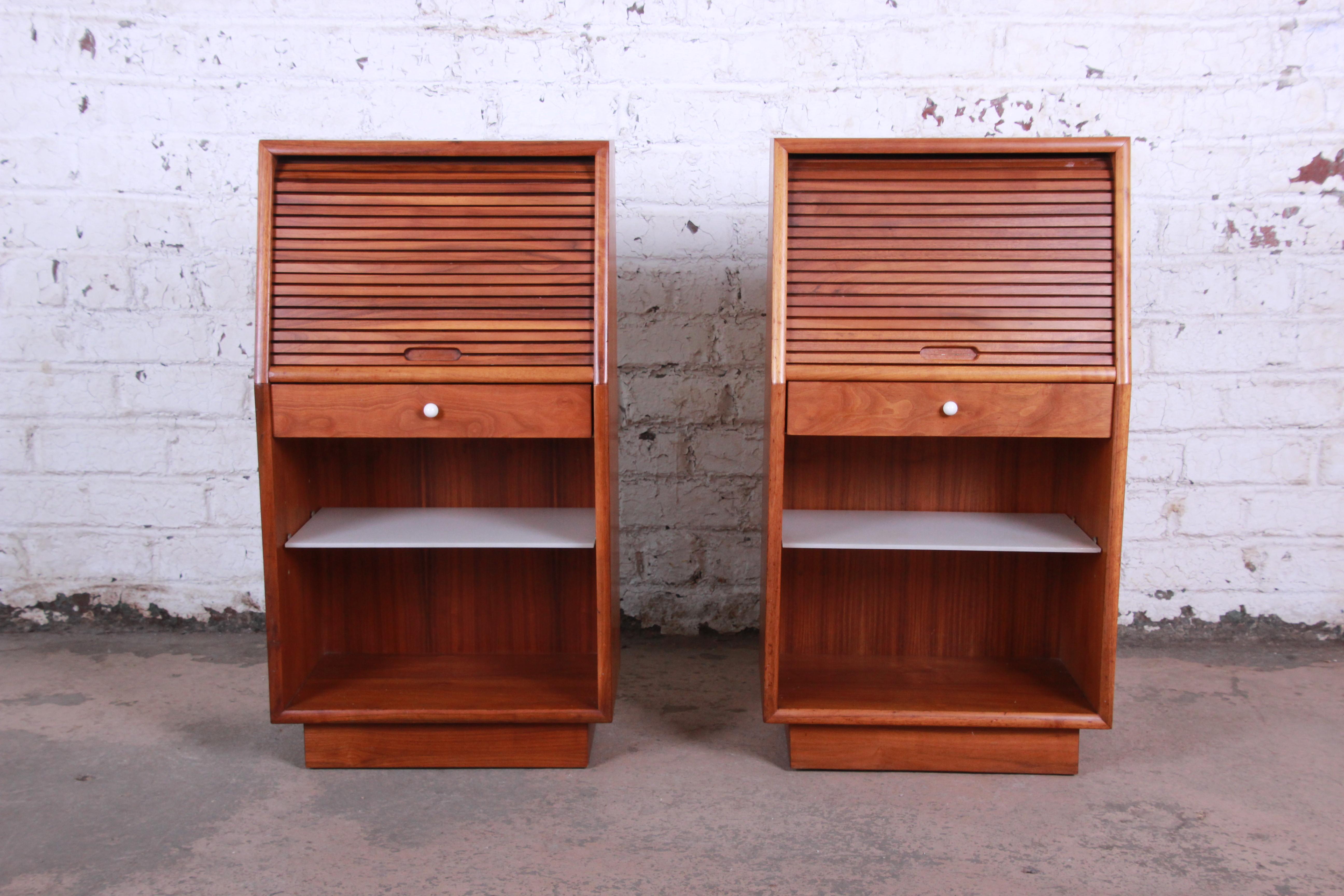 An excellent pair of Mid-Century Modern walnut tambour door nightstands designed by Kipp Stewart for Drexel Declaration. The nightstands feature gorgeous walnut wood grain and sleek midcentury design. They offer good storage, each with an open