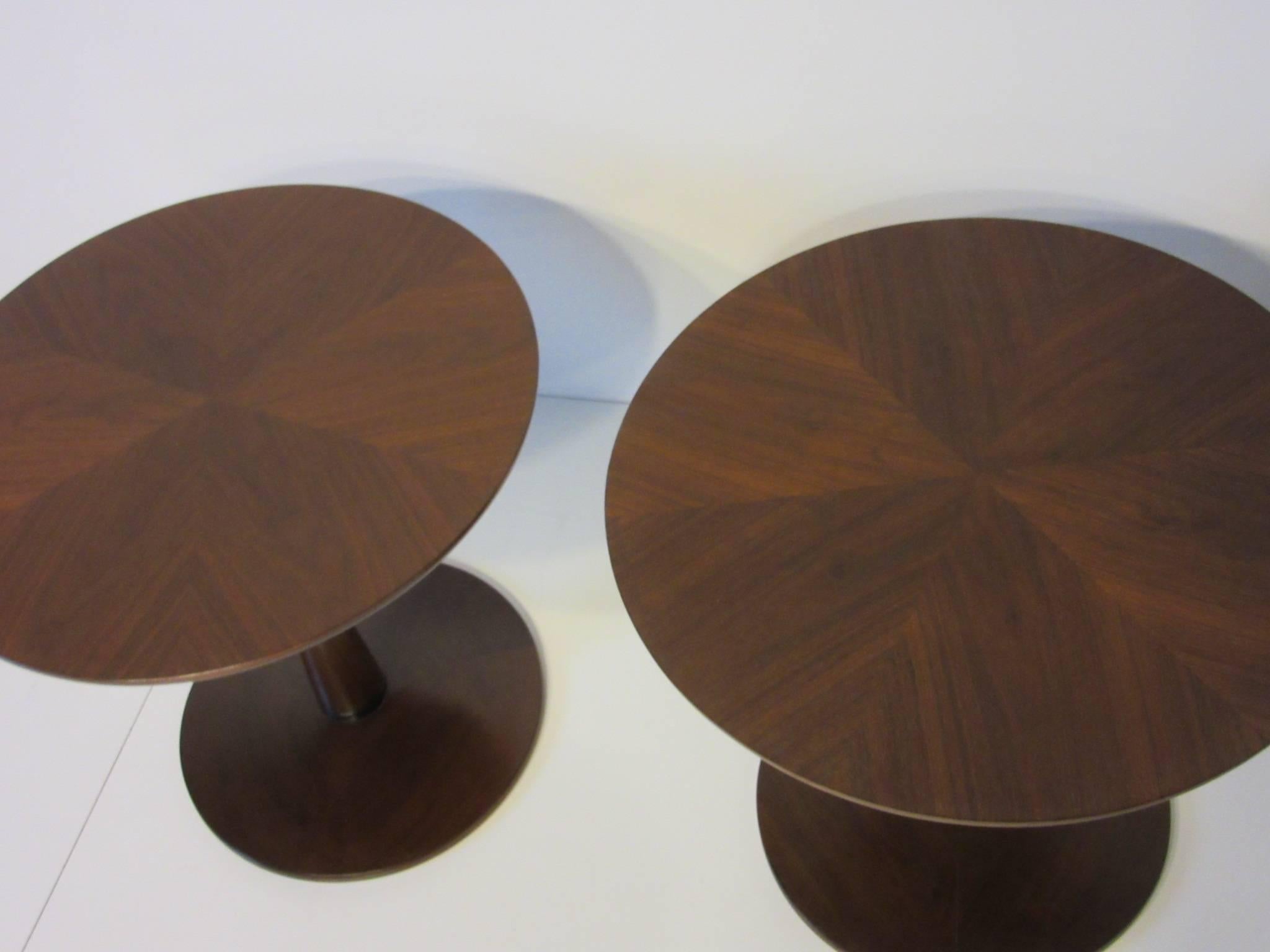 A pair of walnut pedestal side tables with great grained book matched walnut surface a curved top edge and round base with black ebony detail. Manufactured by the Drexel Furniture company for the Declaration collection.