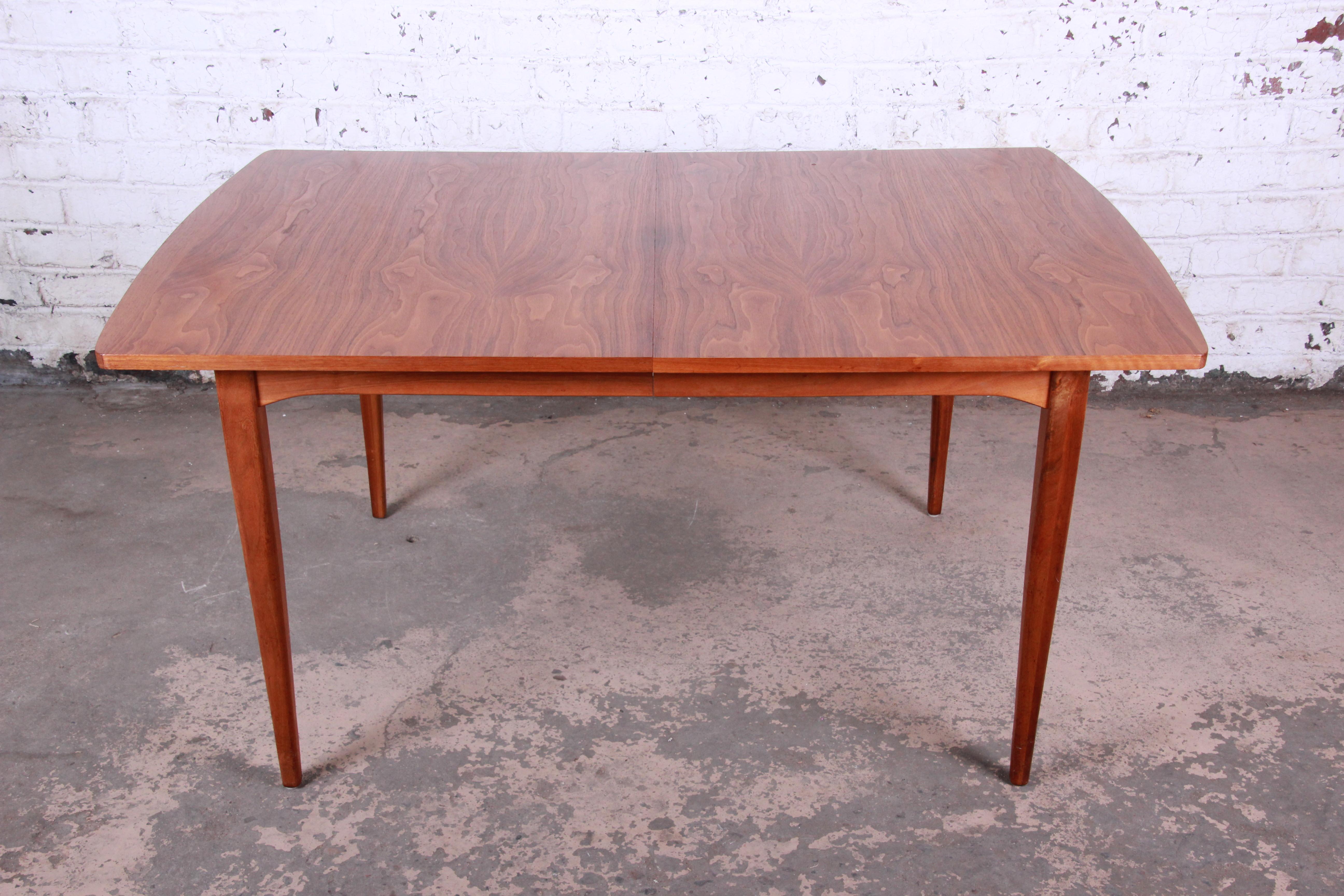 A gorgeous Mid-Century Modern walnut extension dining table designed by Kipp Stewart for his Declaration line for Drexel. The table features stunning walnut wood grain and sleek midcentury design. It measures 60