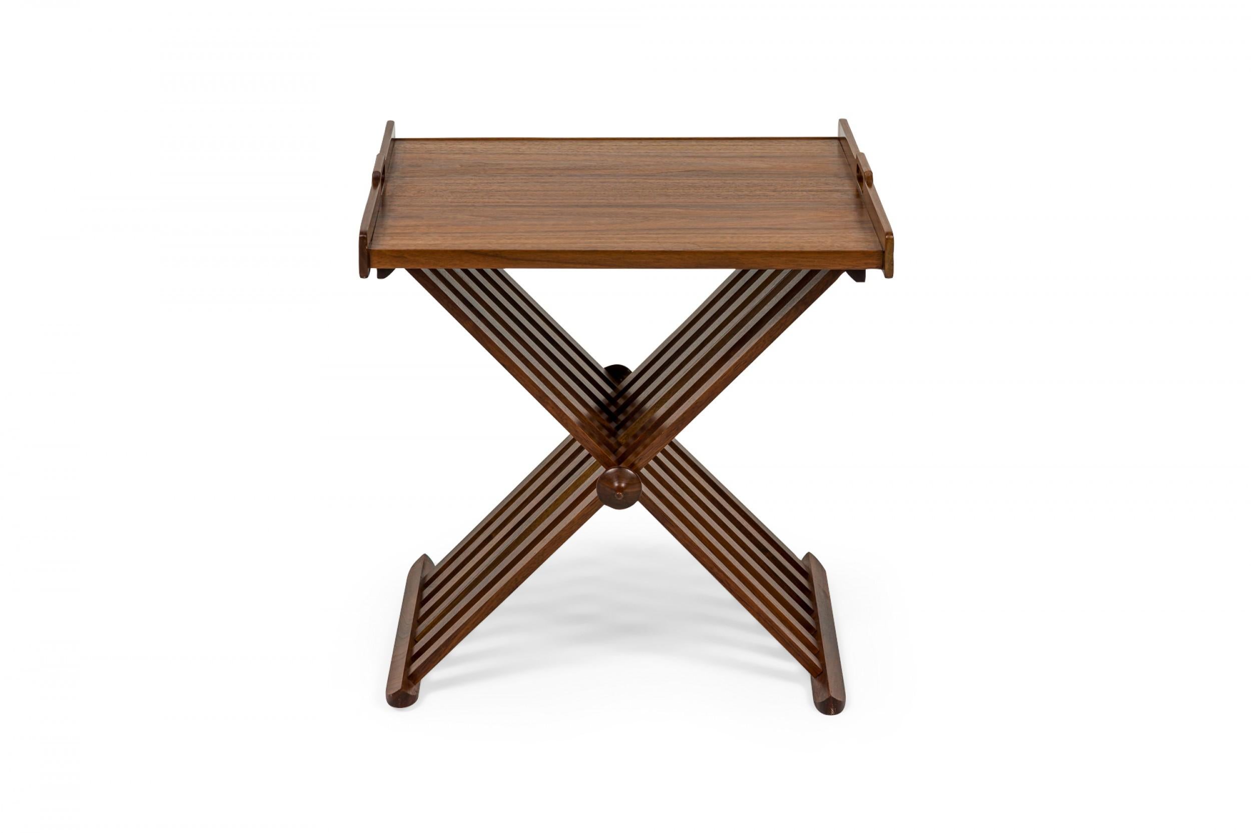 American Mid-Century wooden end / side tables with removable tray tops with two low sides with bracket-shaped cutout handles and folding X-form bases comprised of wooden slats. (KIPP STEWART FOR DREXEL FURNITURE COMPANY).