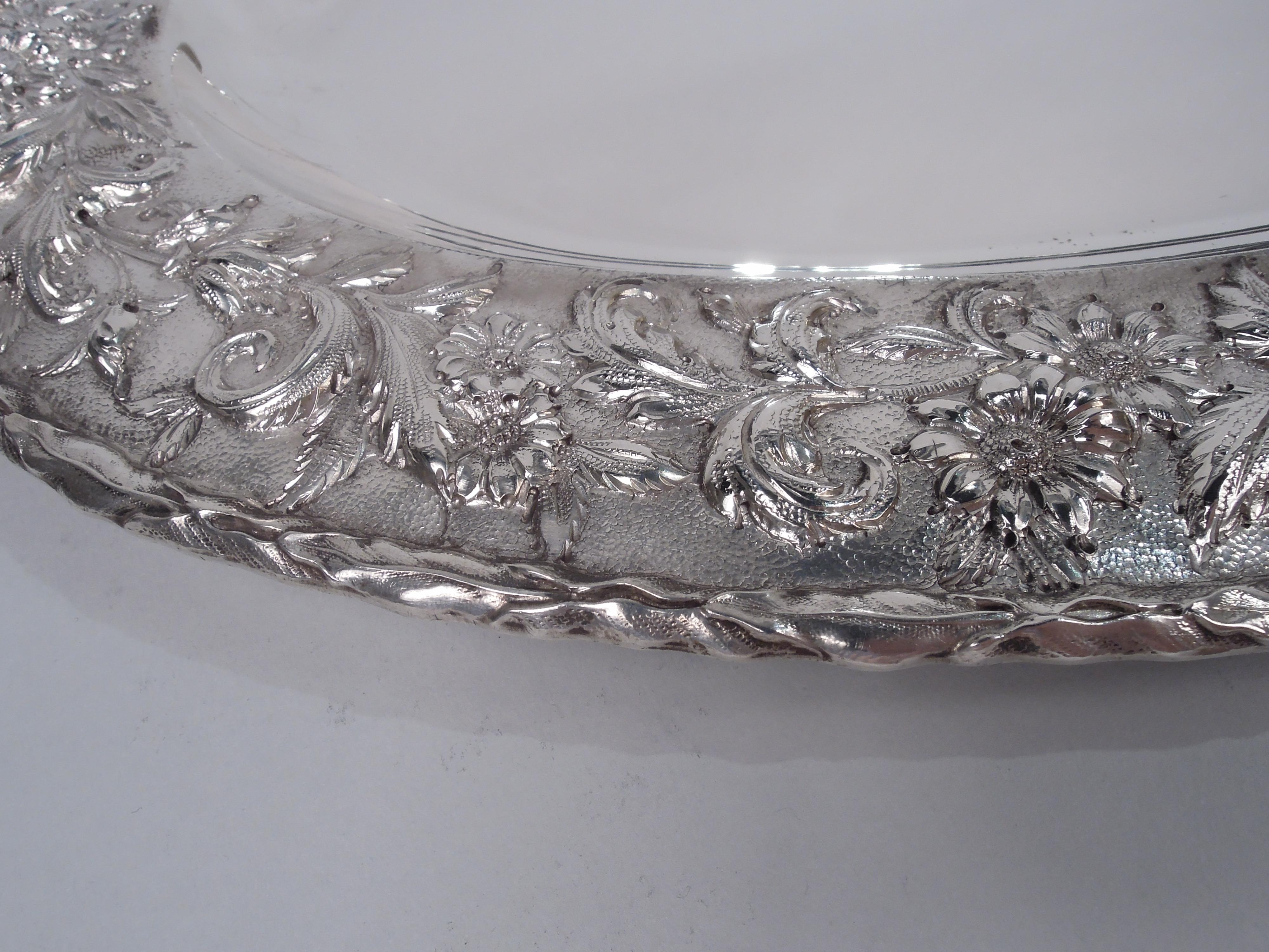 Edwardian sterling silver tray. Made by S. Kirk & Son Inc. in Baltimore. Oval well and wide shoulder with repousse floral garland on stippled ground; imbricated leaf rim. Fully marked including maker’s stamp (1925-32), no. 2517, and phrase “Hand