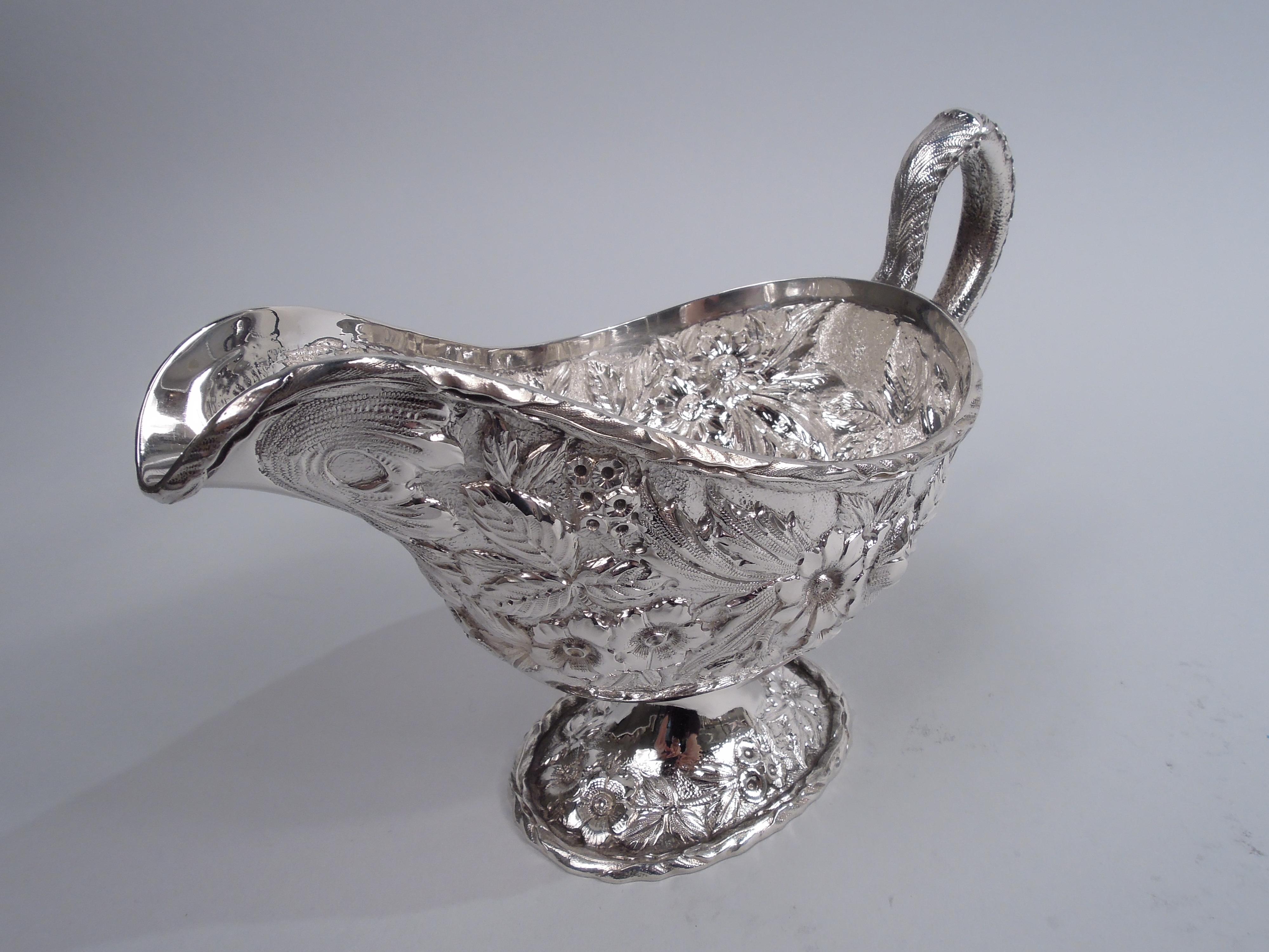 Edwardian sterling silver gravy boat. Made by S. Kirk & Son in Baltimore, ca 1940. Ovoid with helmet mouth and raised oval foot; dense floral repousse on stippled ground. Cast leaf-capped and -mounted high-looping handle with low-relief flowers.