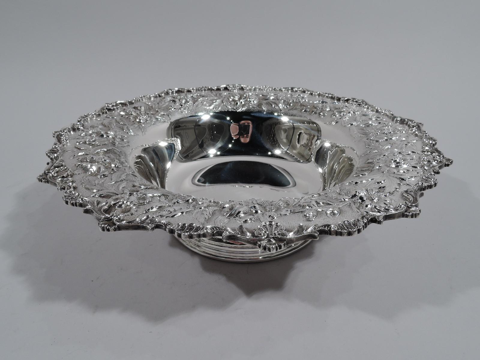 Pretty sterling silver bowl. Made by S. Kirk & Son in Baltimore. Plain well with tapering sides and raised and spread foot. Wide and gently curved shoulder with repousse floral garland on stippled ground. Rim has applied scallop shells, leaves, and