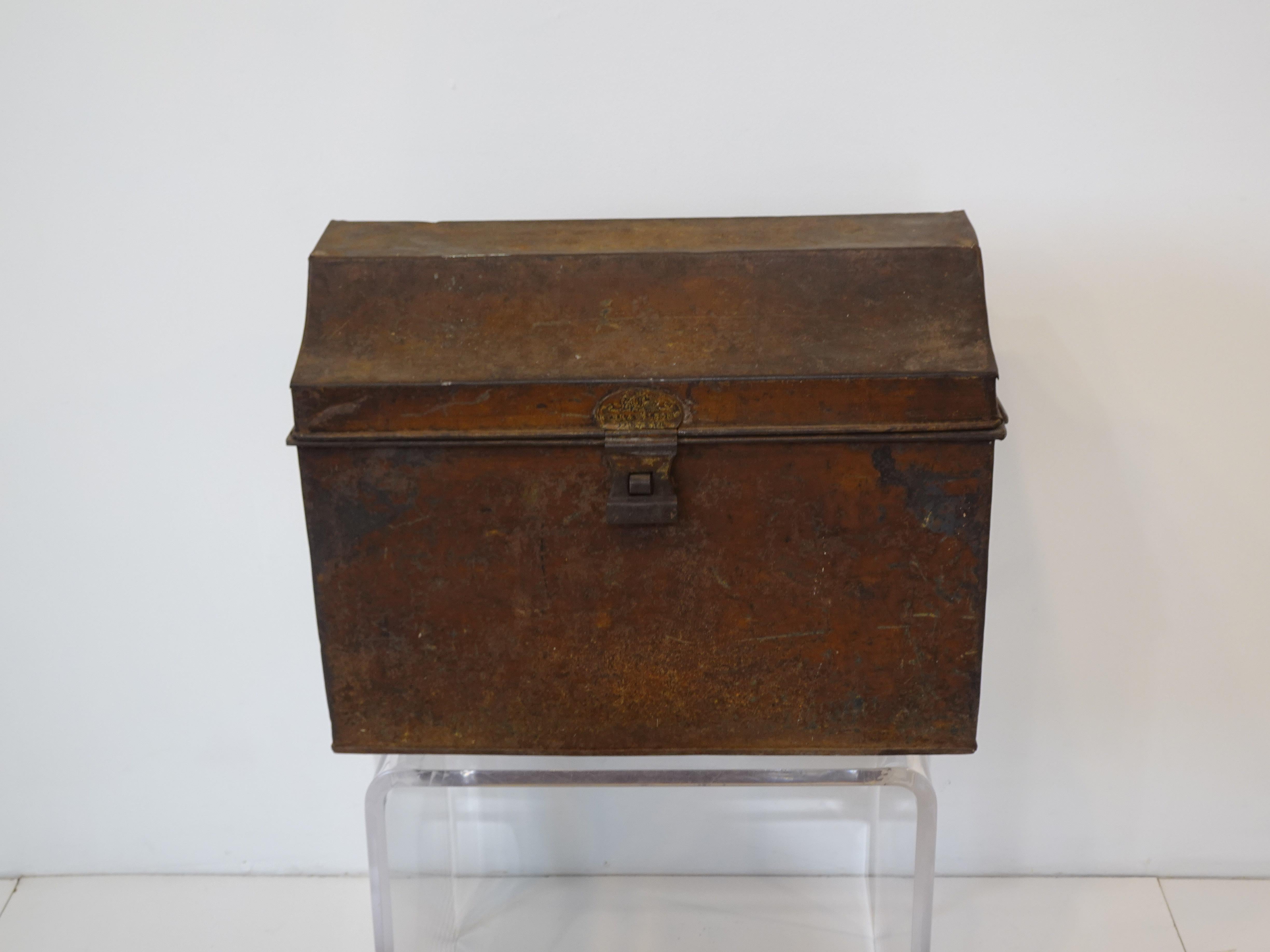 A small metal Royal mail box or trunk with sarcophagus styled design having a latch to the front and steel handles to each side. Above the latch is the embossed label for the manufacturer Kirk & Wilsons made in England, the outside has great aged