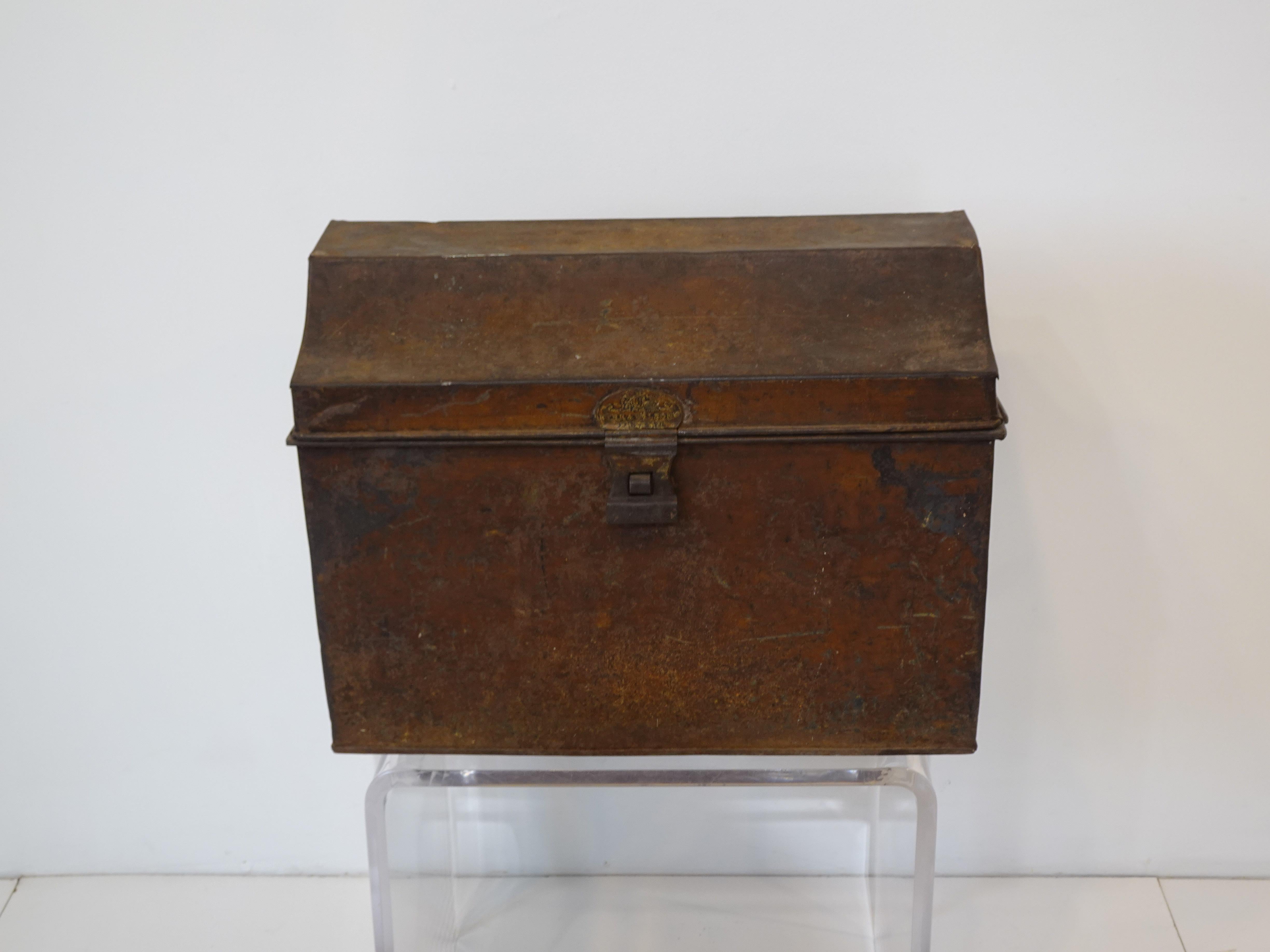 A small metal Royal mail box or trunk with sarcophagus styled design having a latch to the front and steel handles to each side. Above the latch is the embossed label for the manufacturer Kirk & Wilsons made in England, the outside has great aged