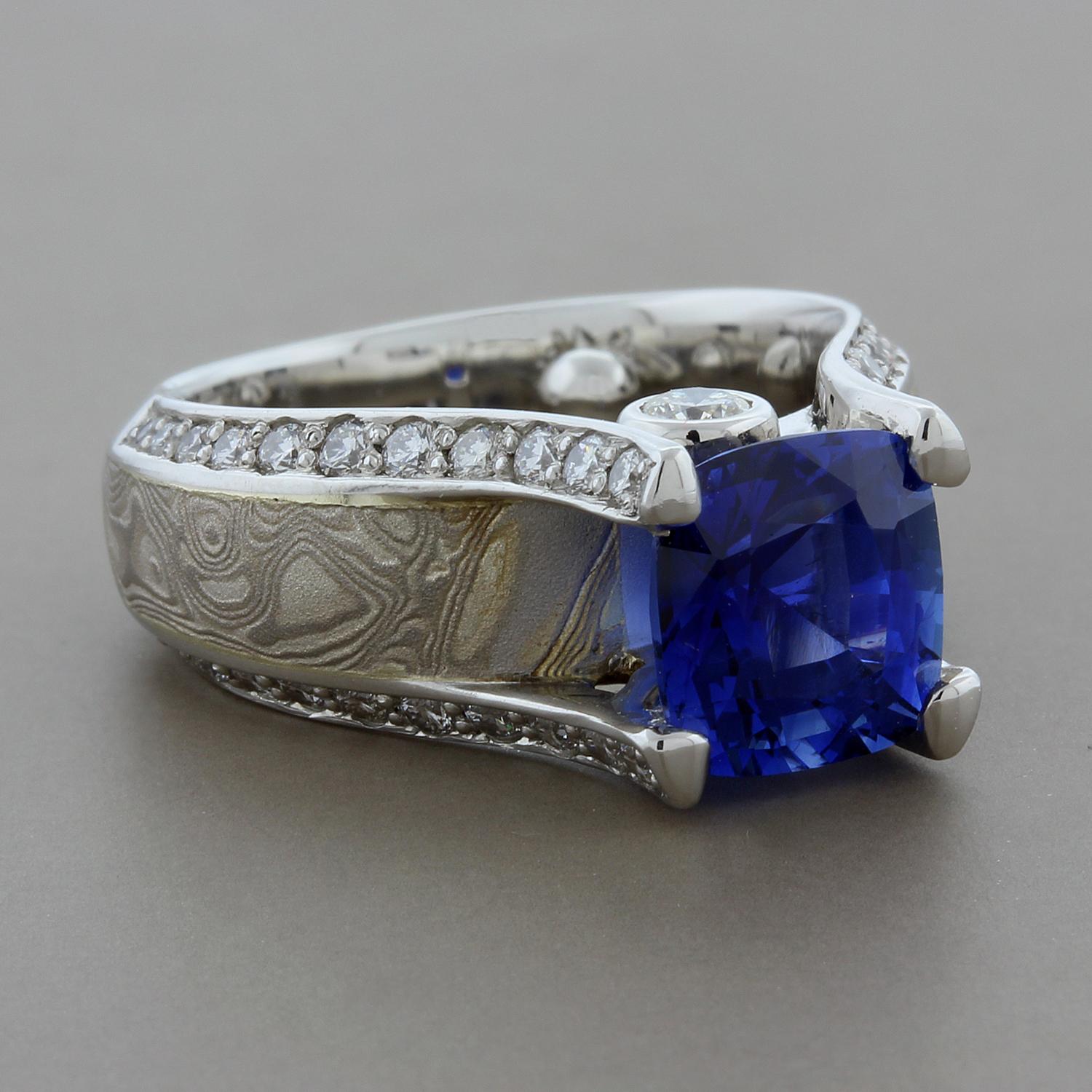 Kirkawa presents a ring featuring a 2.60 carat cushion cut vivid blue sapphire with 0.70 carats of white diamond accents. This striking ring is set in platinum and 14K white gold with a silver band in the center of the shank. The silver band