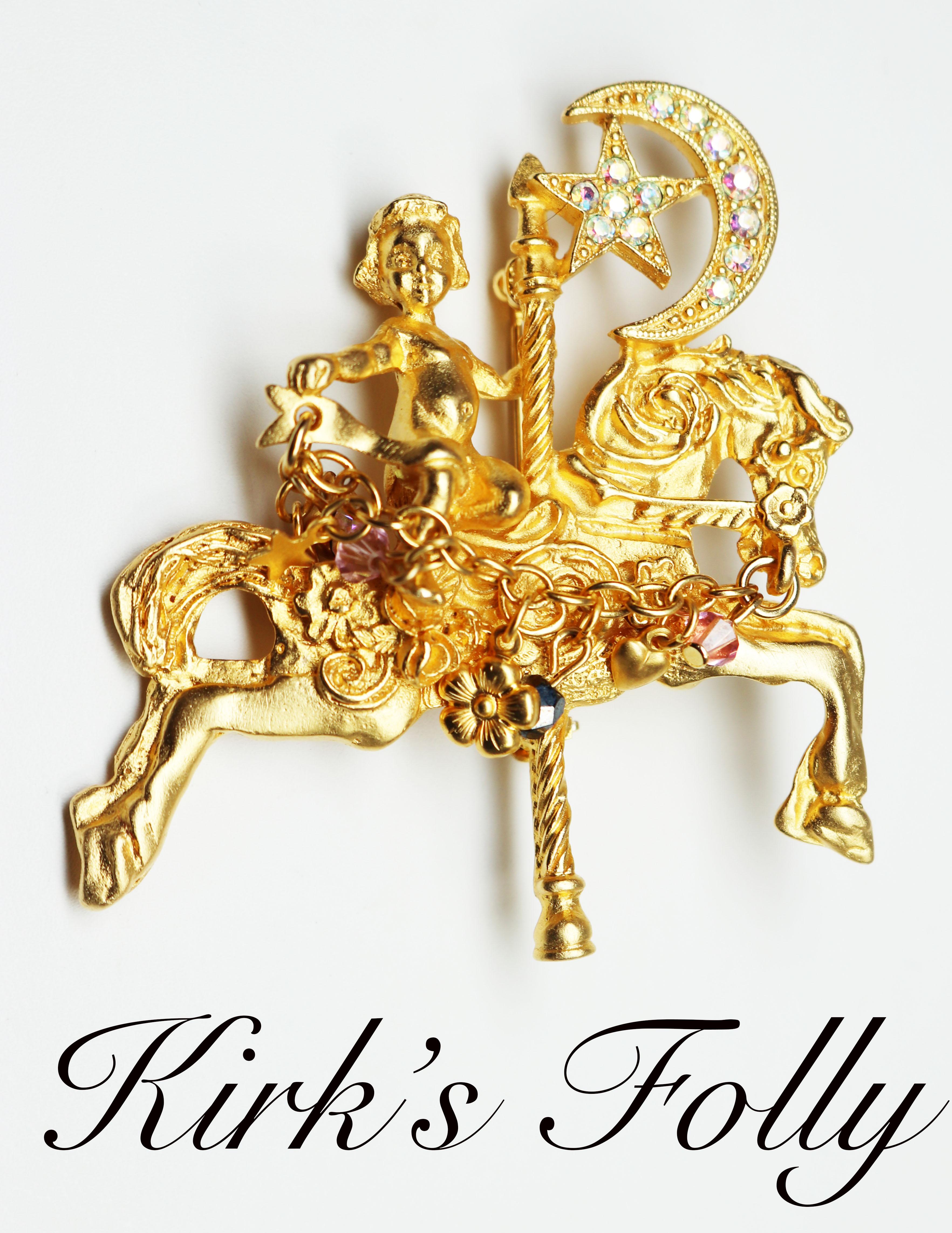 This brooch is one of Kirk Folly's most famous pieces with a decadent, magical look. It features bright aurora borealis stones encrusted in the magical celestial charms adorning an angel riding a golden carousel horse. There is a decorative chain