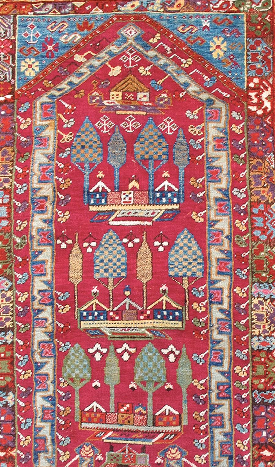 Questo coloratissimo tappeto da preghiera proveniente dall'area di Kirshehir, nell'Anatolia settentrionale, dipinge l'immagine ripetuta di un cortile con cipressi. Una nicchia di preghiera - o mihrab - è delineata in blu con zig-zag geometrici,