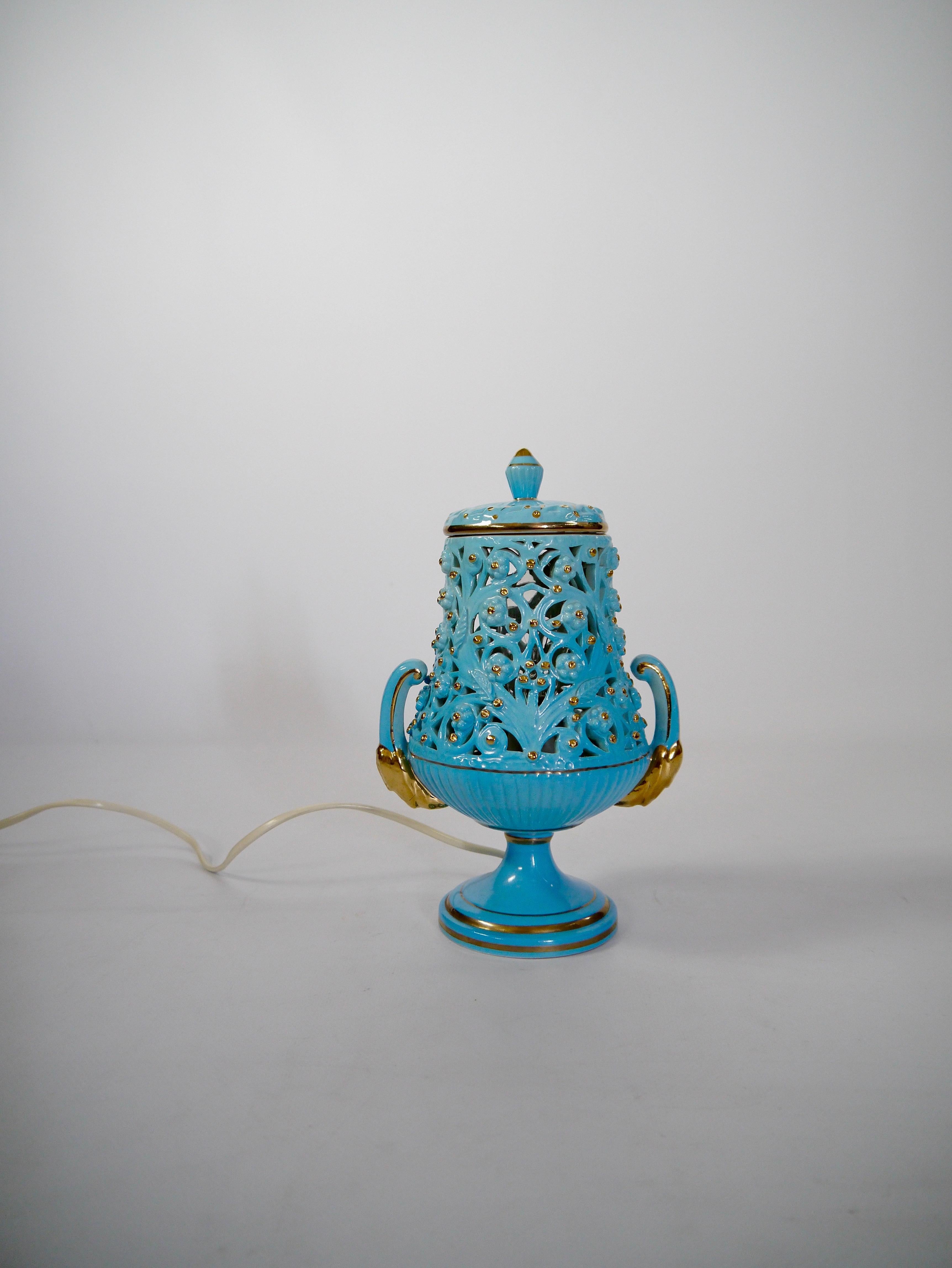 Lampada kitsch in ceramica italiana, che imita un'urna con manici e coperchio, realizzata negli anni '60. Azzurro brillante con intarsi dorati, motivo organico traforato che lascia trasparire la luce creando un'esposizione di ombre e luci che