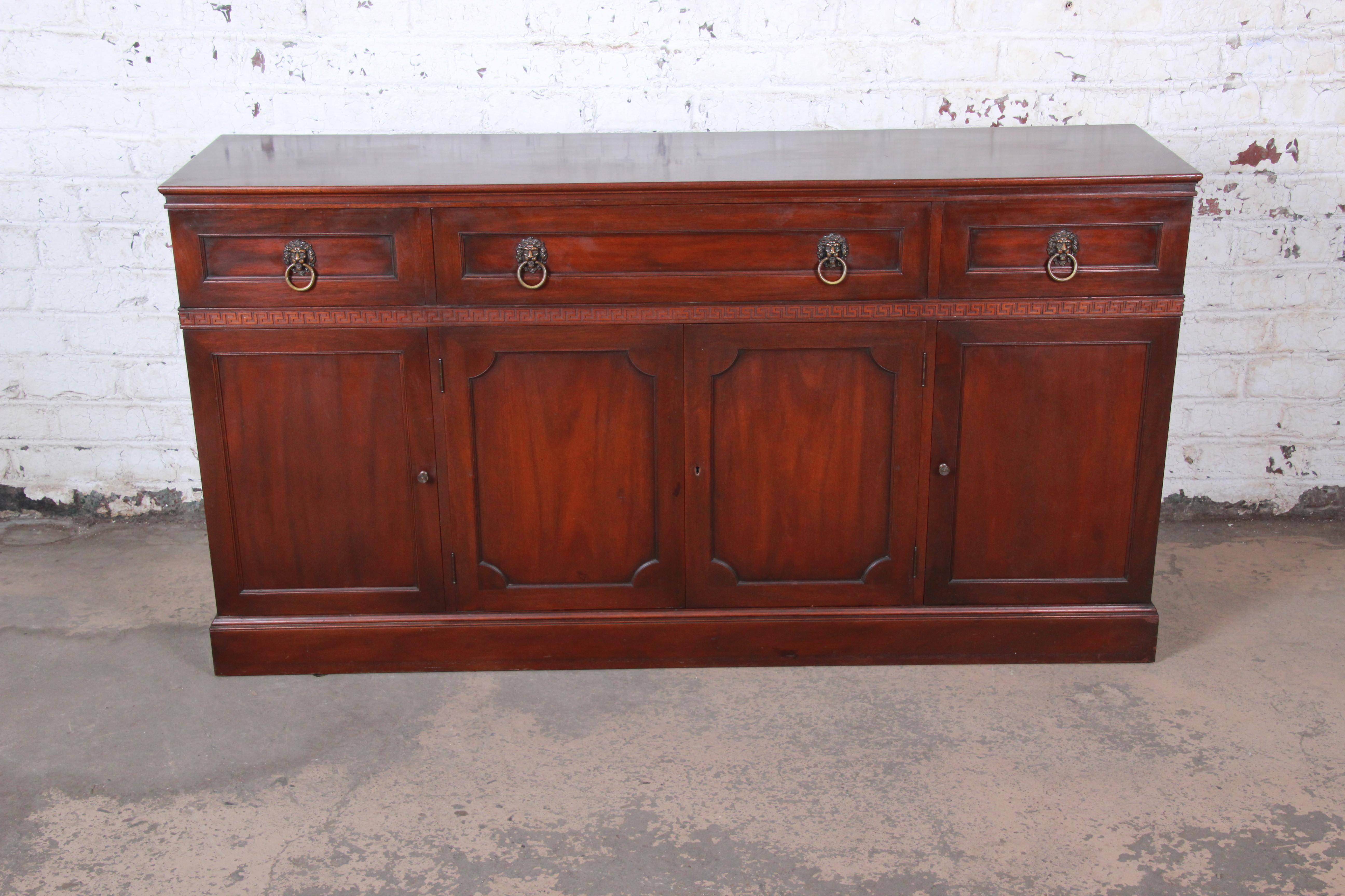 An exceptional carved mahogany Regency sideboard credenza or bar cabinet by Kittinger Furniture. The sideboard features gorgeous mahogany wood grain with a beautiful carved Greek Key design. It offers excellent storage, with three drawers at the top