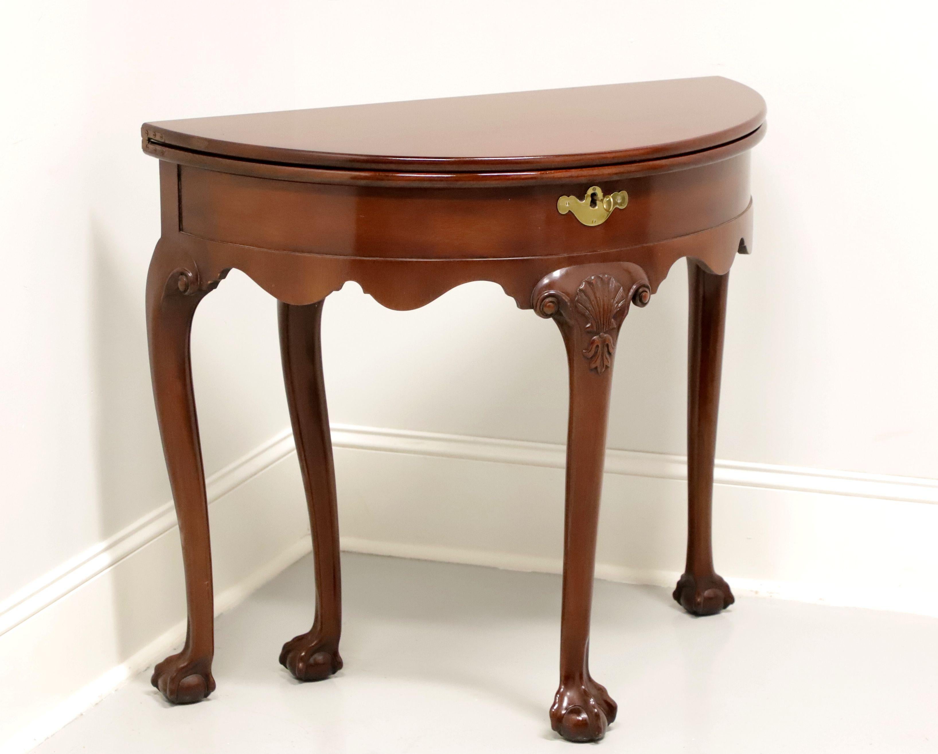 A Georgian style flip-top demilune table by Kittinger Furniture, an authorized reproduction of a Colonial Williamsburg piece. Solid mahogany, brass lock escutcheon, bow front, carved apron, carved knees and ball in claw feet. Back gateleg swings out