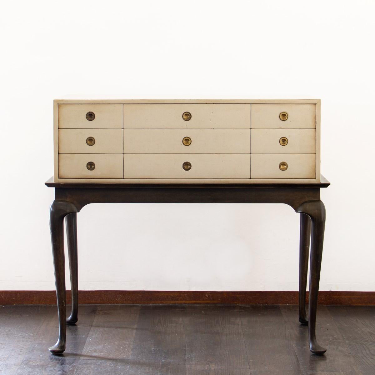 An oyster colored, twelve-drawer cabinet, set on dark wooden, raised cabriole legs. The drawers are furnished with round brass ring pull handles and the interior of the drawer is embossed with makers mark, designed by Kittinger, 1950s.

The