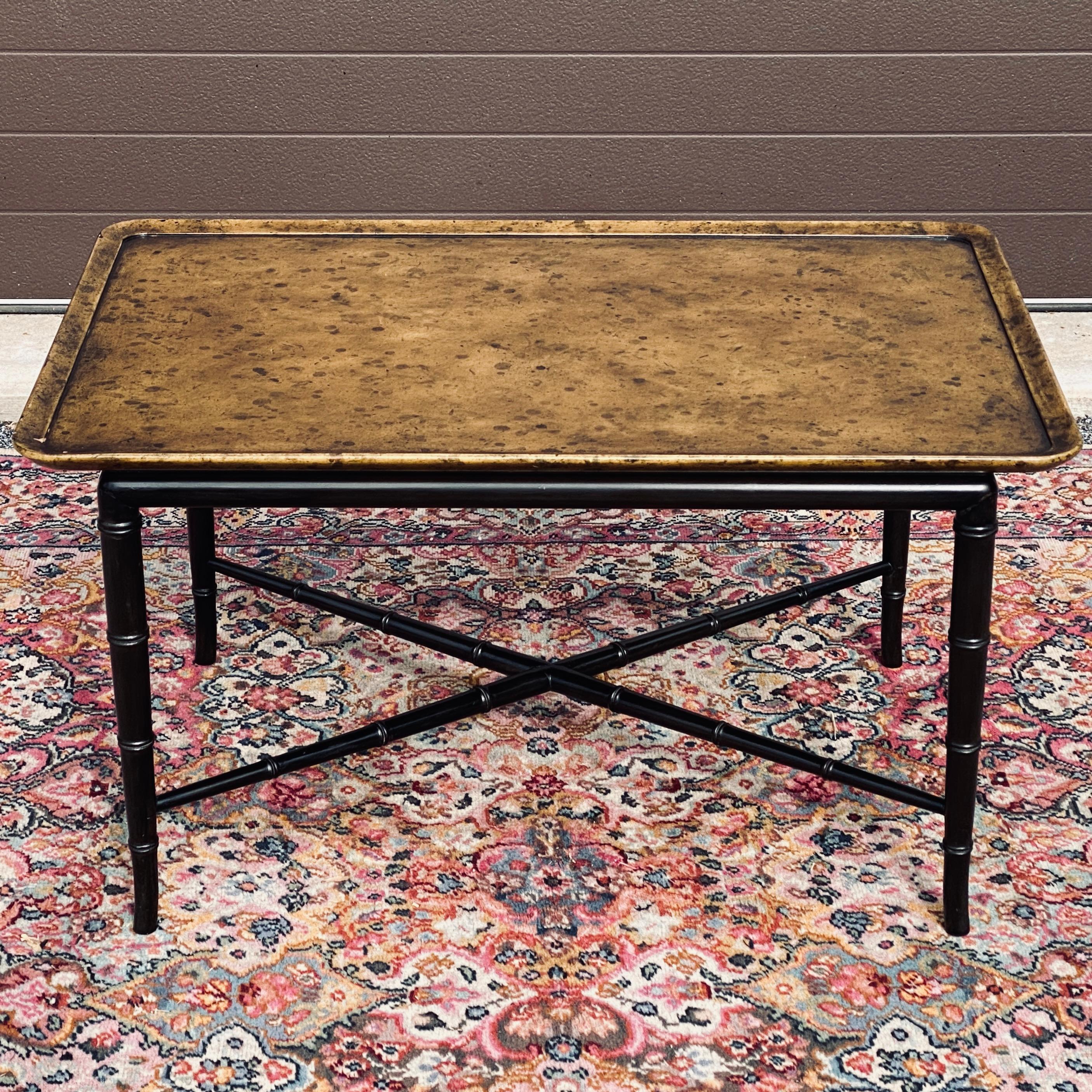 This elegant cocktail table dates to the 1950's and was manufactured by Kittinger Furniture of Buffalo, New York. The tray style top has the original faux tortoiseshell lacquered finish and is attached to an ebonized faux bamboo base of four tapered
