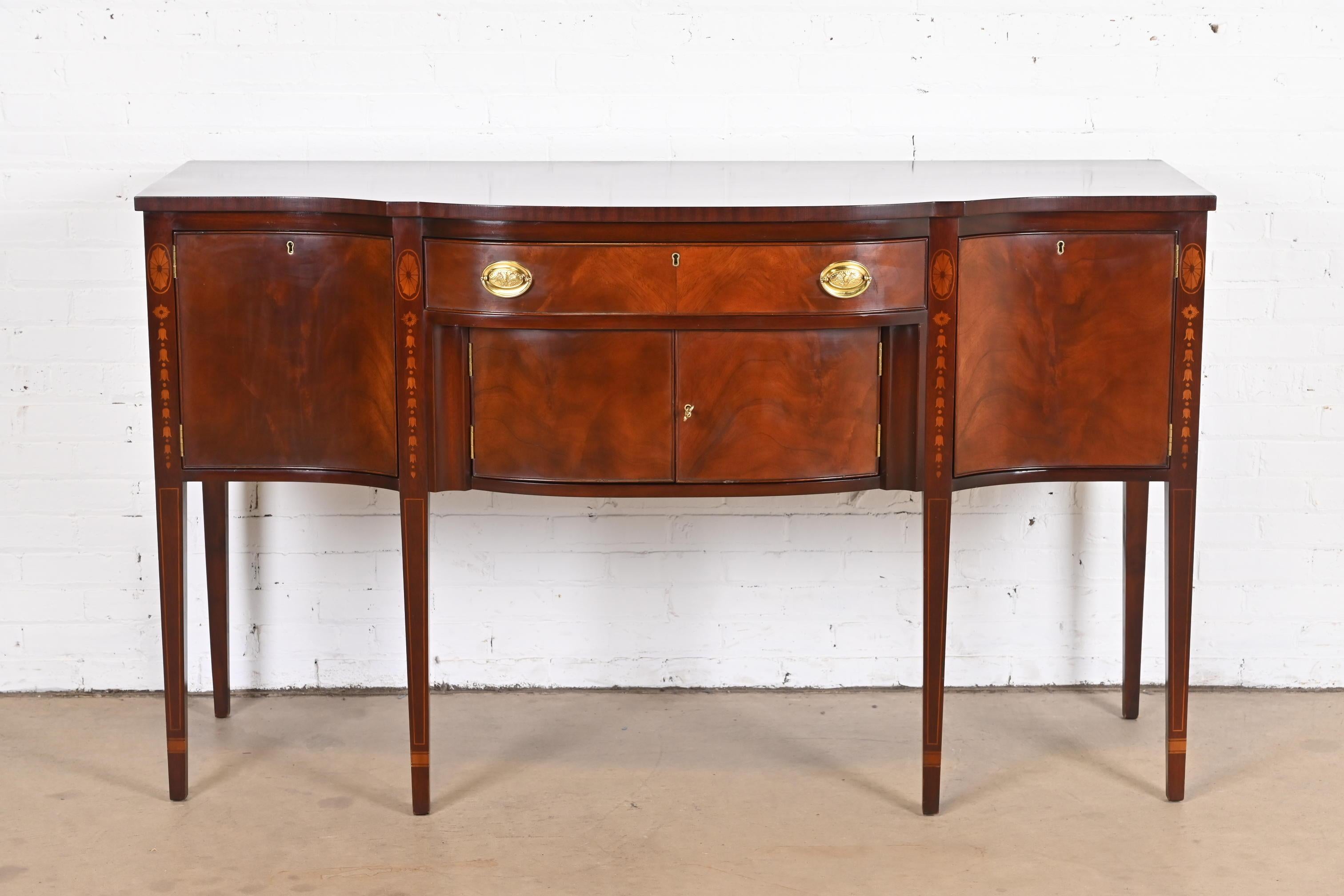 A gorgeous Federal or Hepplewhite style bow front sideboard buffet or credenza

By Kittinger

USA, Circa 1980s

Flame mahogany, with inlaid satinwood marquetry, and original brass hardware.

Measures: 66