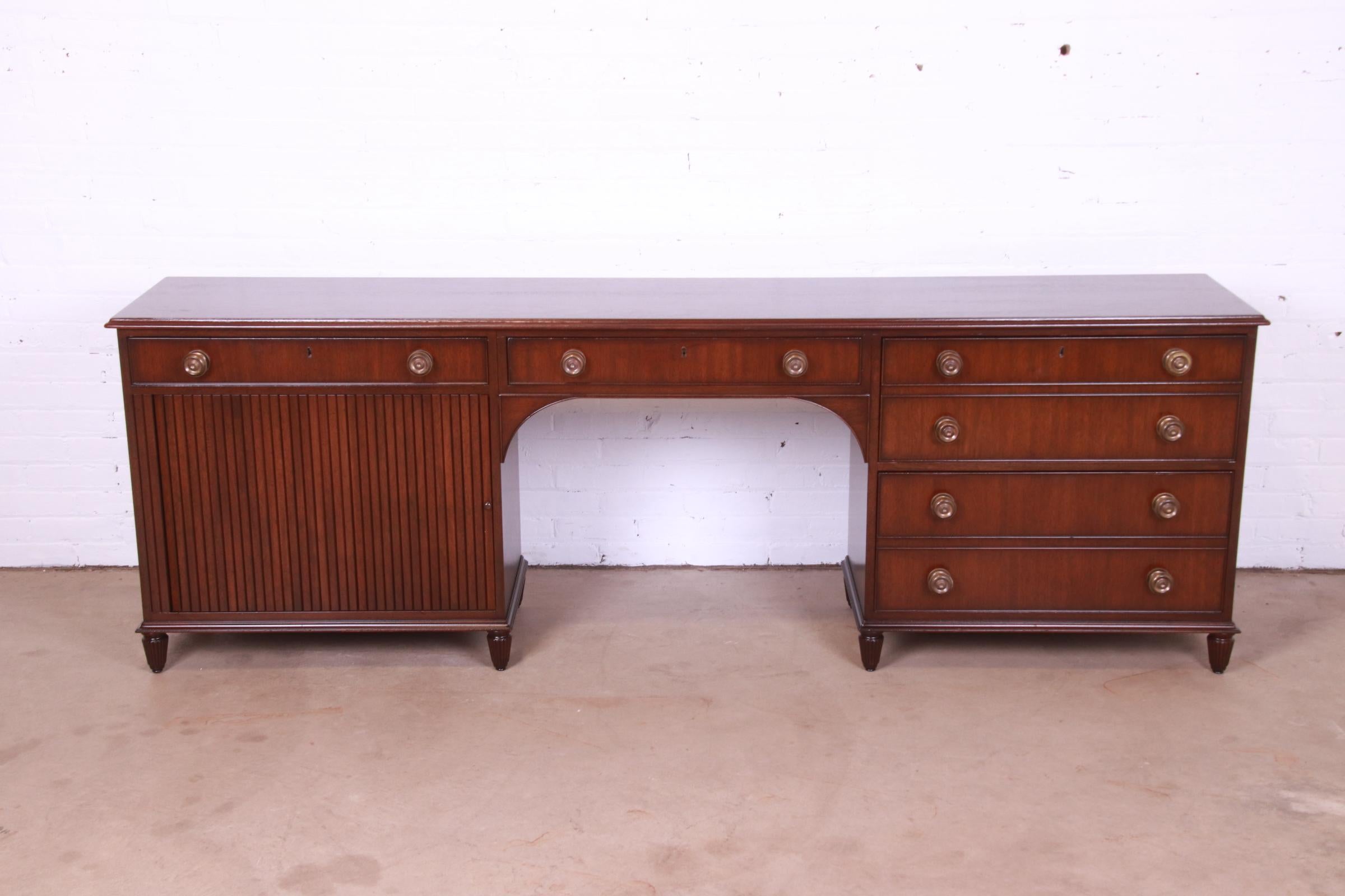 A stately Georgian style executive credenza desk with tambour door.

By Kittinger

USA, mid-20th century

Carved mahogany, with original brass pulls.

Measures: 91.5