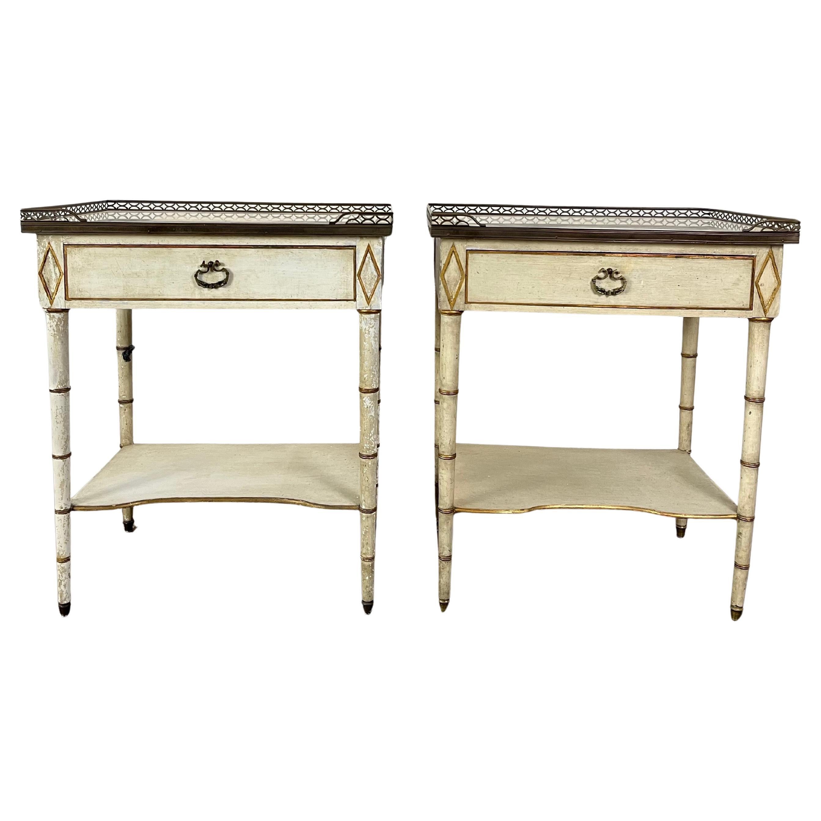 A pair of Louis XVI style nightstands or end tables designed by Kittinger Furniture Co. in the mid 20th century. Each table features a pierced brass gallery surrounding a white and gray veined marble top, a pull out drawer, four ivory-painted faux