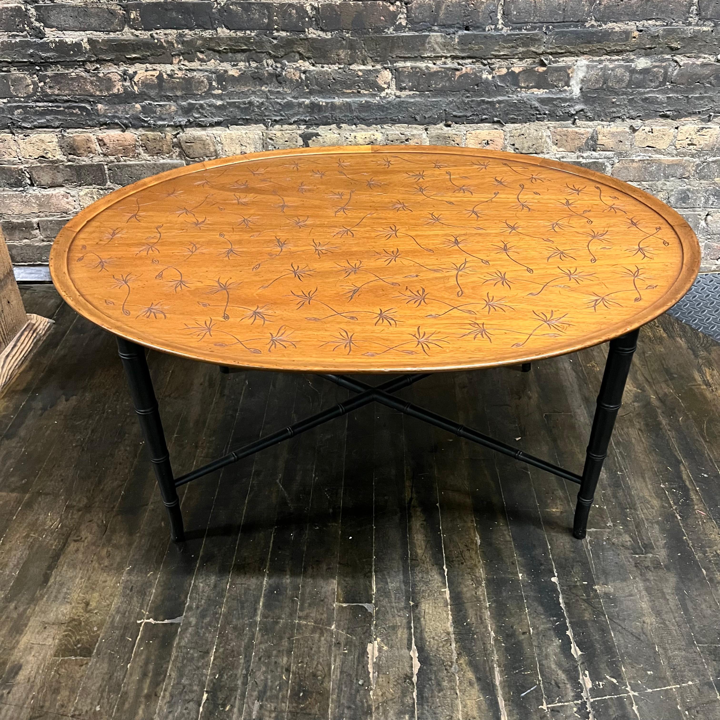 Lovely midcentury coffee table by Kittinger Furniture Company (Buffalo, NY). This oval table has a lovely walnut top that is incised with a dandelion pattern (in black). The black lacquered base has a faux bamboo styling with an x stretcher between