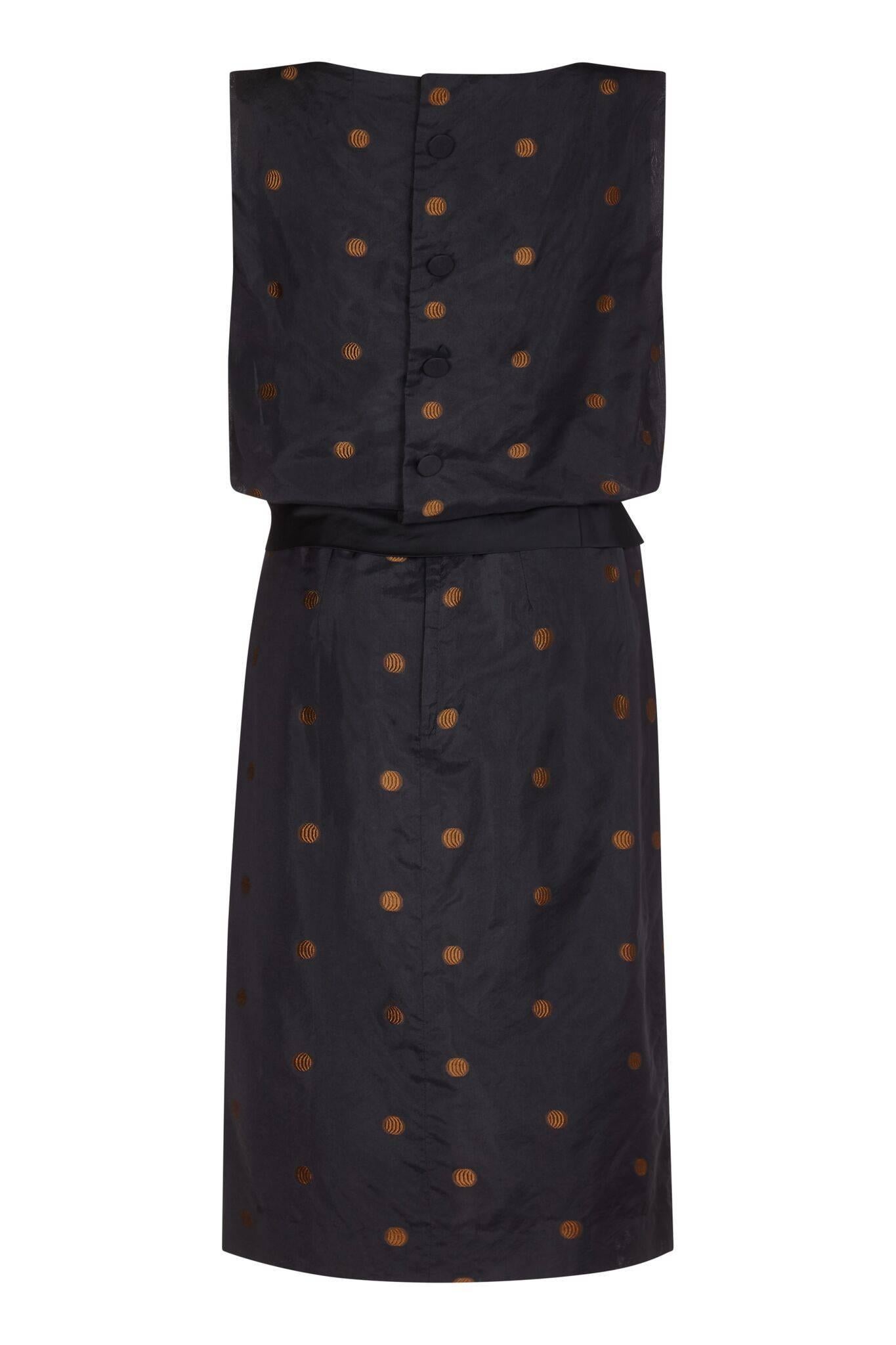 This stylish vintage 1950s Kitty Copeland black silk taffeta dress with polkadot detail and peplum sash boasts timeless city chic and unusual design features. The taffeta overlay has a playful machine embroidered bronze polkadot motif to contrast