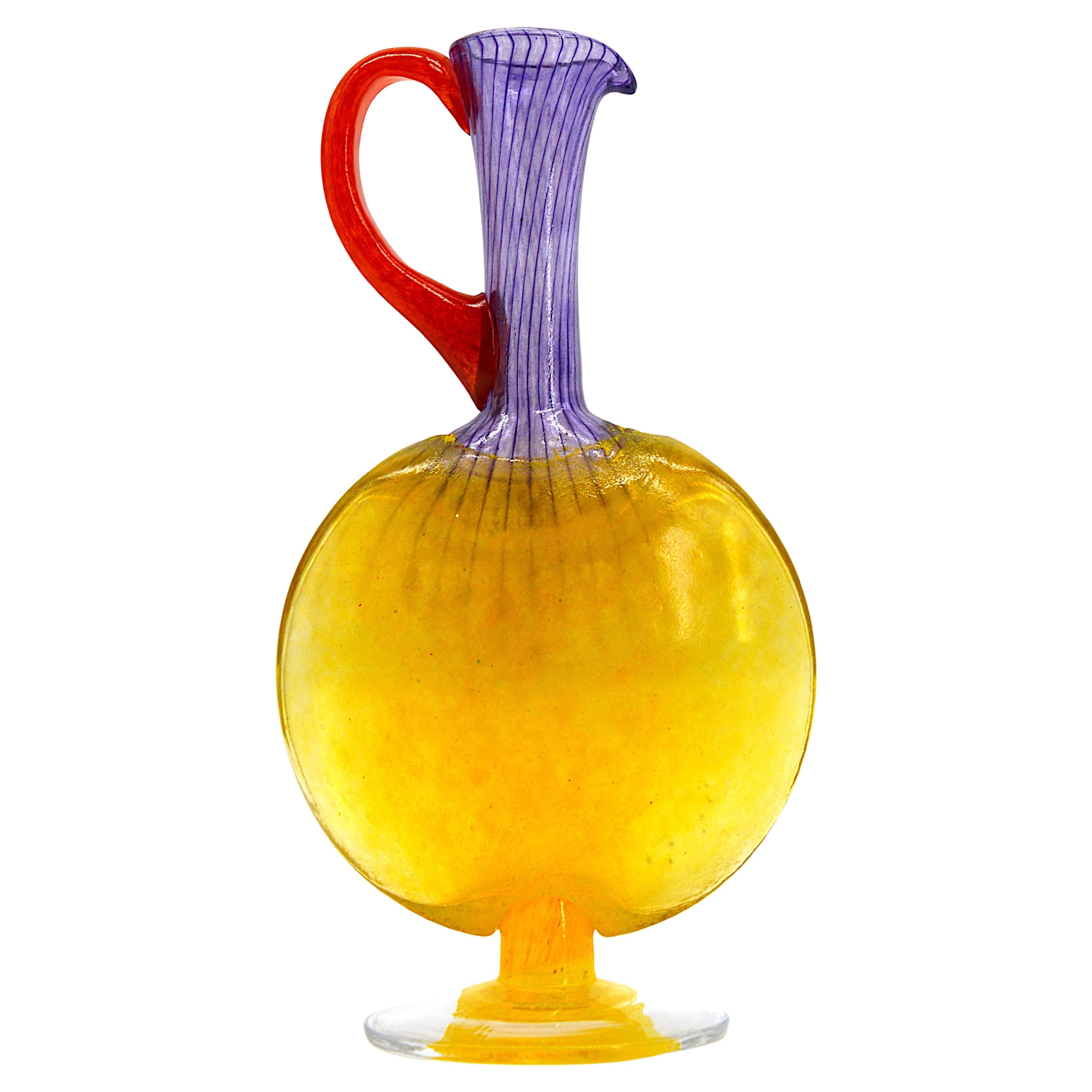 Art glass carafe by Kjell Engman at Kosta-Boda, Sweden, late 1990s. Filigree glass with yellow base and body, purple neck and red handle. Measures: Height 9.5