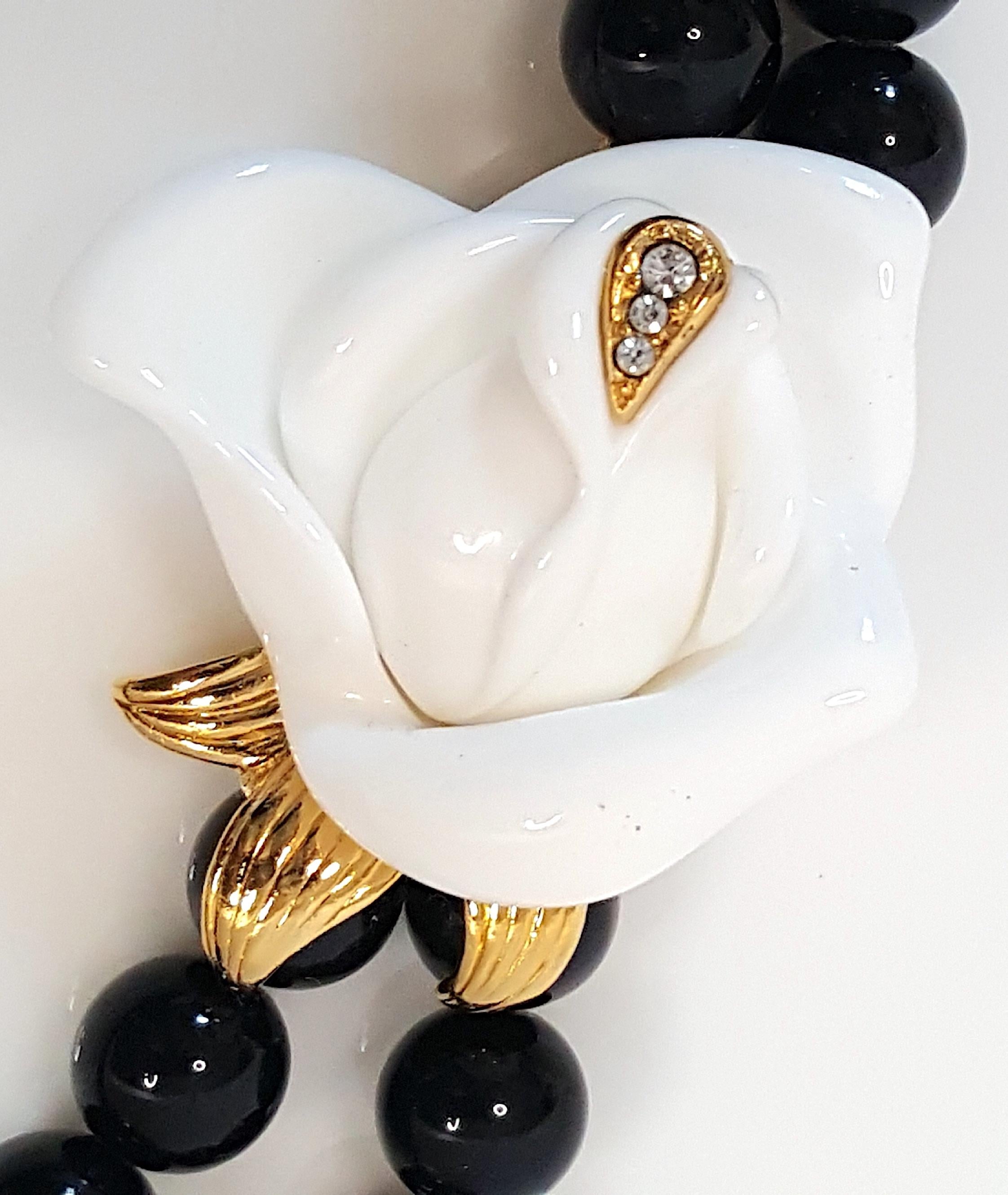 Kenneth Jay Lane, dont le monogramme KJL est signé sur le fermoir en or décoré de rose blanche de ce collier en résine à double brin de perles noires, n'est que l'un des quatre créateurs de bijoux cités par le Brooklyn Museum Costume Collection At
